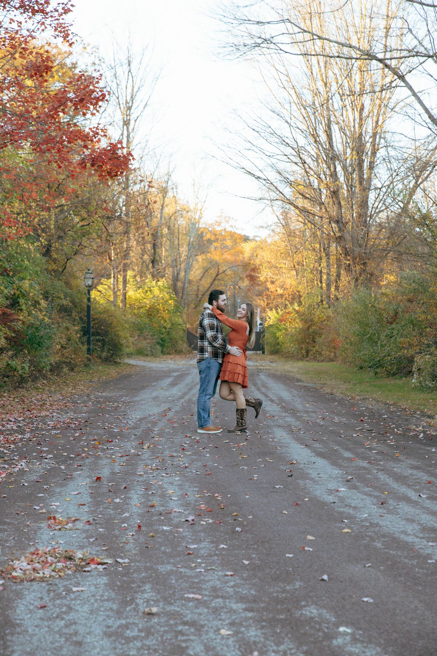 Couple dancing joyfully on a rural road surrounded by vibrant autumn foliage trees.