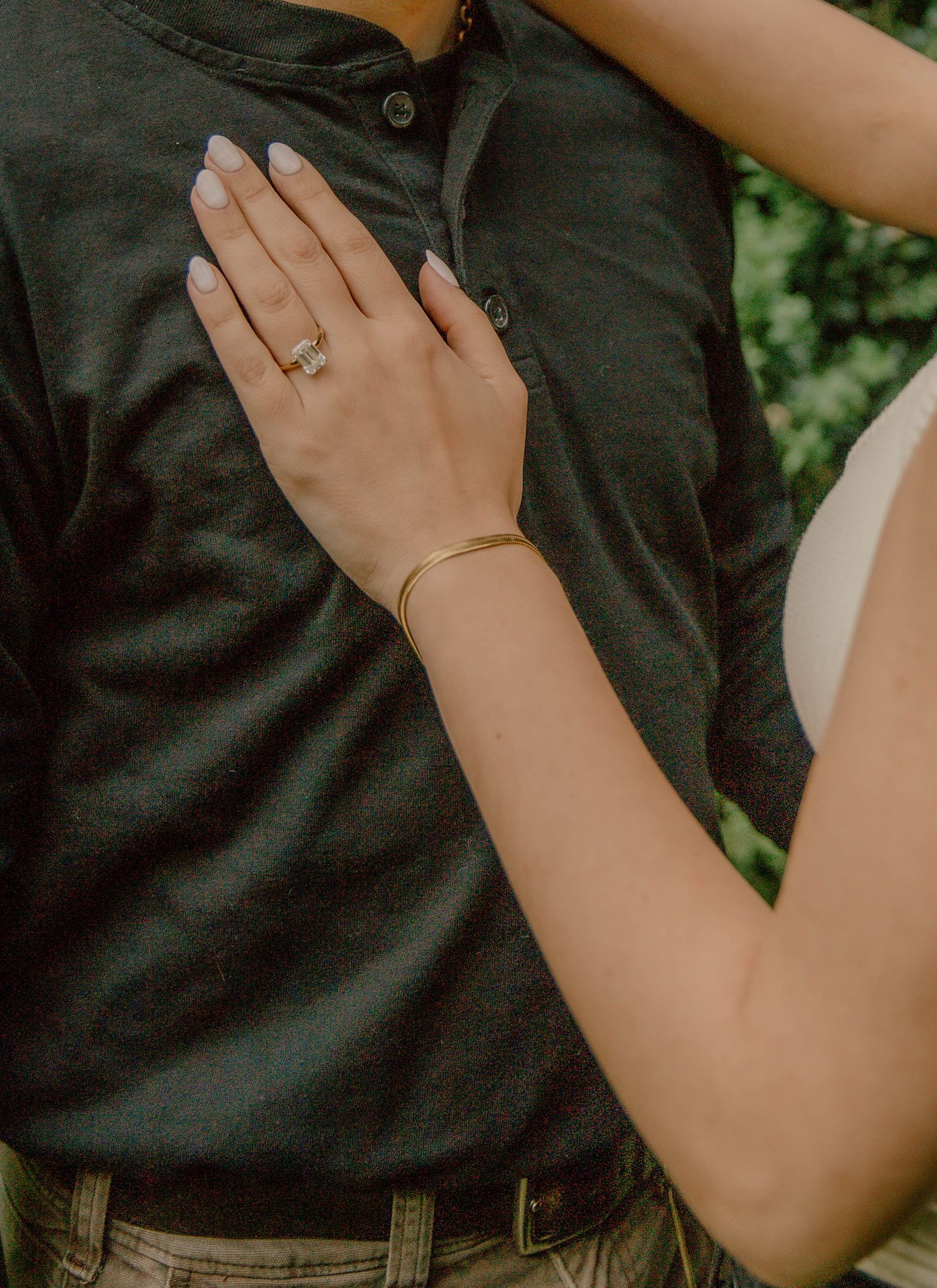 A woman wearing a gold bangle and engagement ring places her hand on a mans chest.
