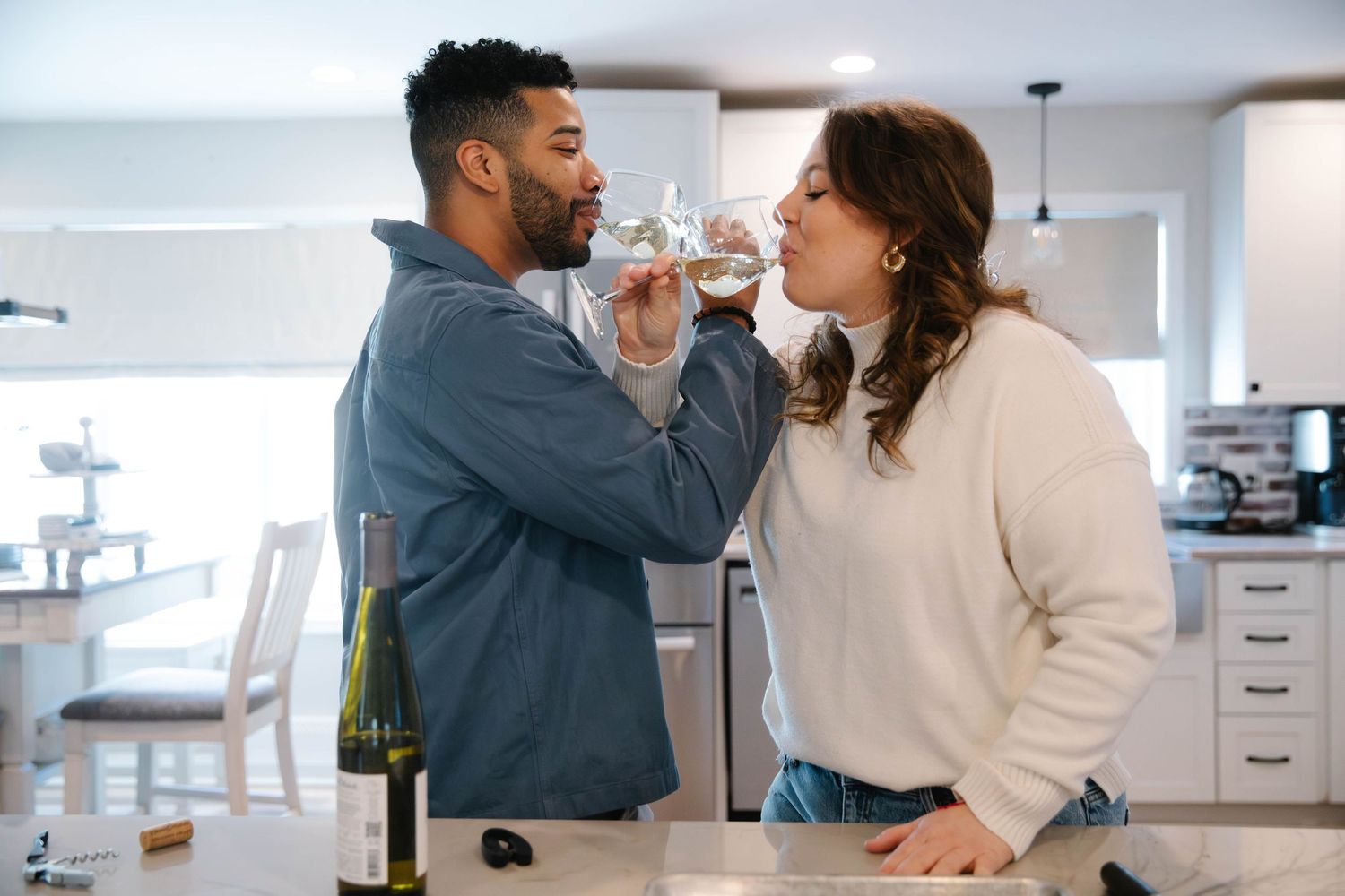 Happy couple sharing wine together at a kitchen counter in a bright modern home.