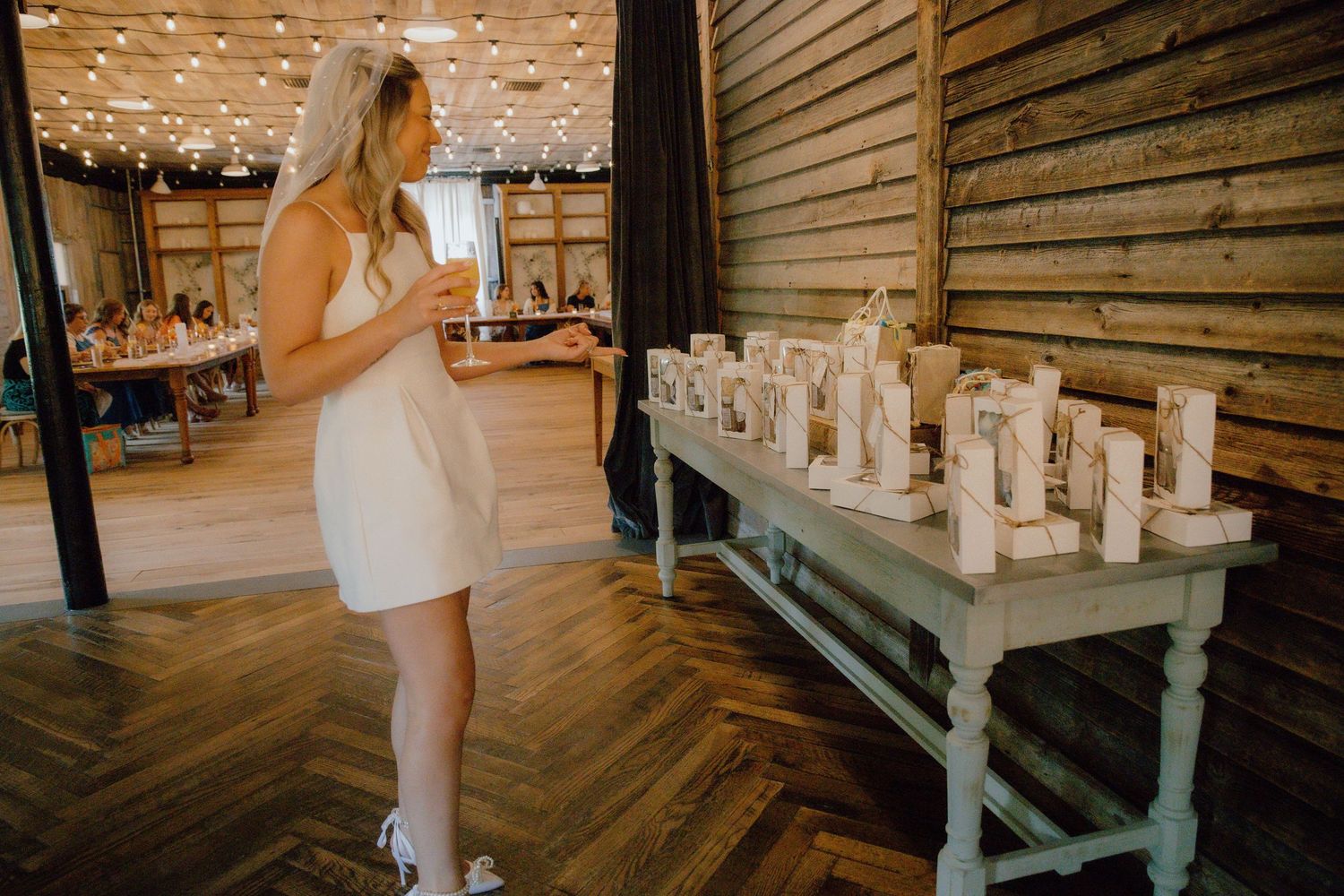Woman in white dress playing Jenga at a rustic barn wedding reception with wooden block tower on table.