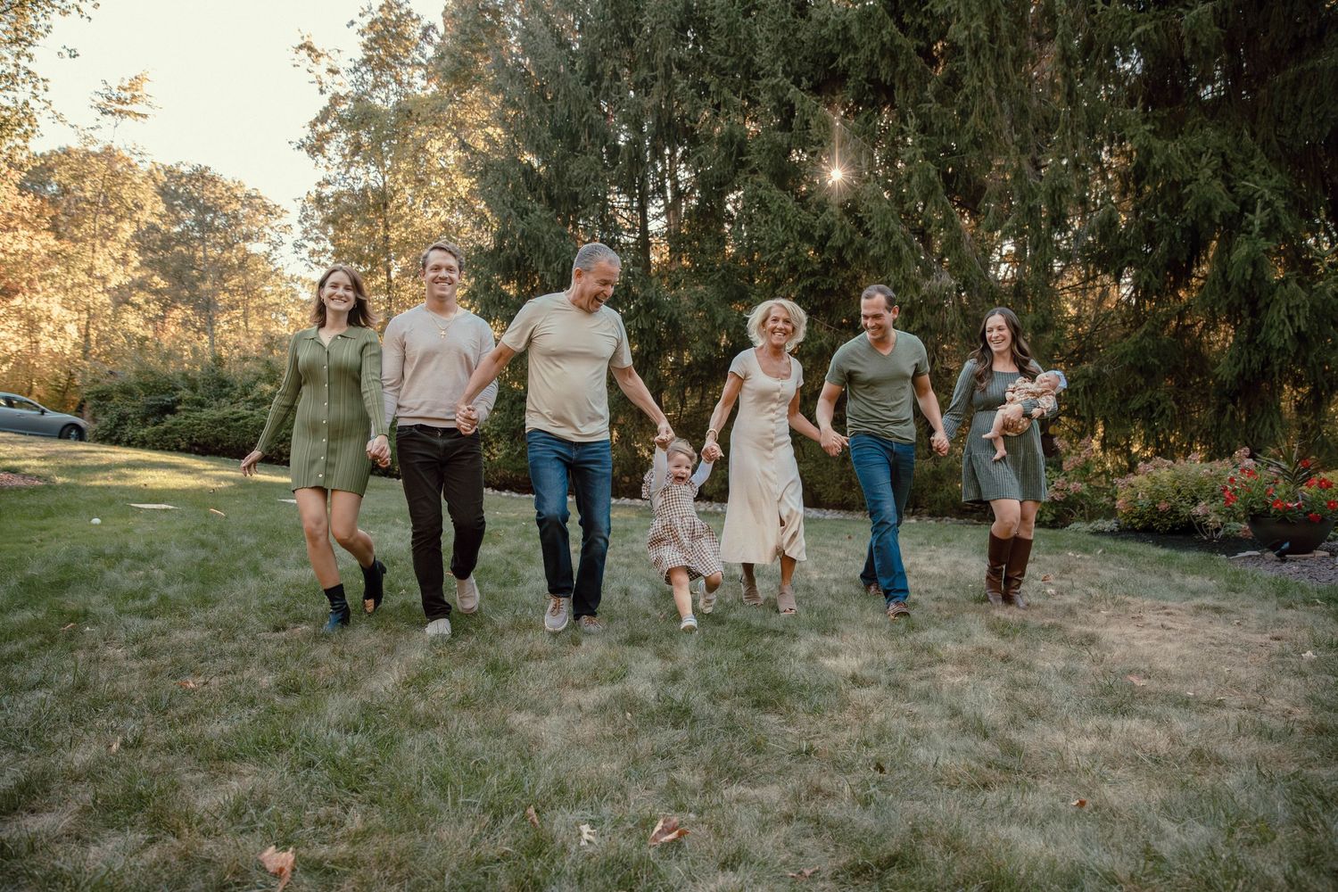 Happy extended family walking together in lush green park during golden hour sunset.