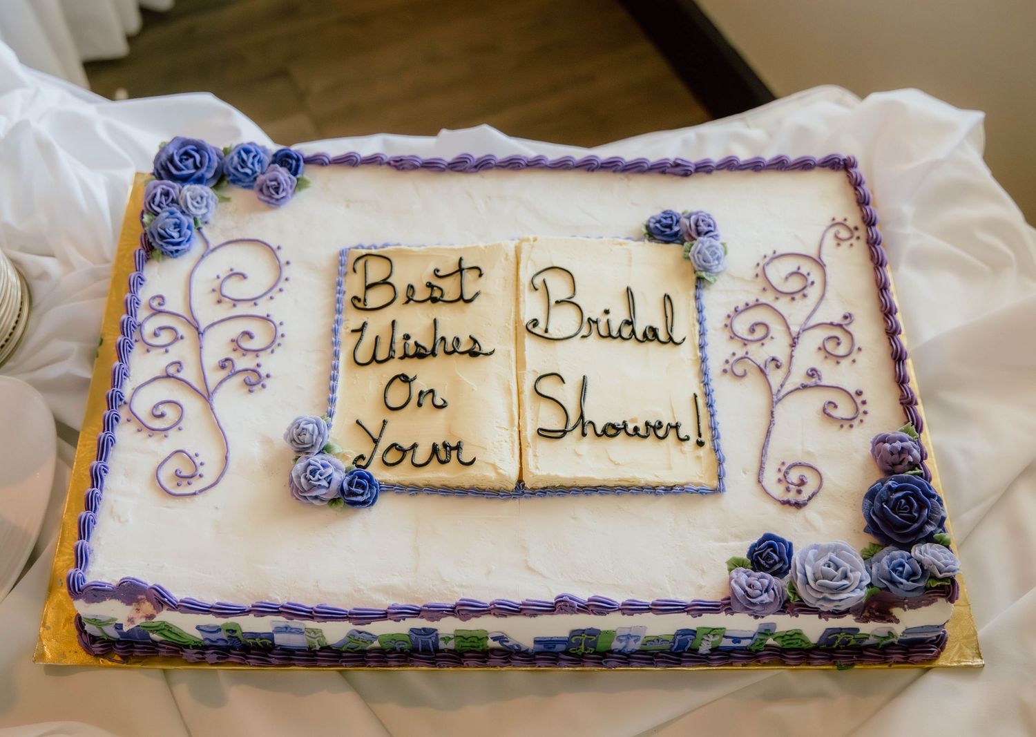 White bridal shower sheet cake with purple roses, decorative swirls, and open book design reading Best Wishes on Your Bridal Shower.