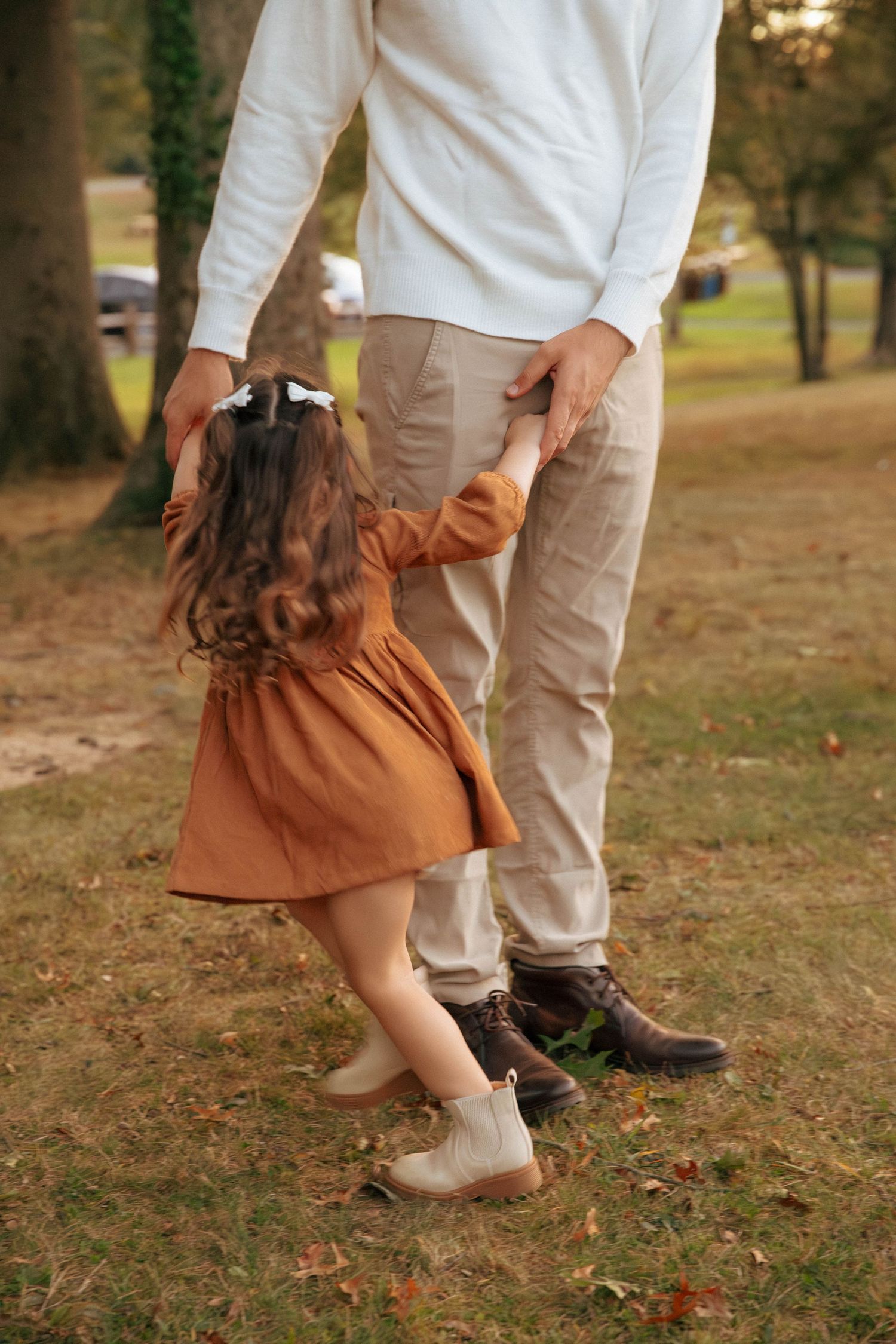 Young girl in rust dress holding her fathers hand while walking in an autumn park.