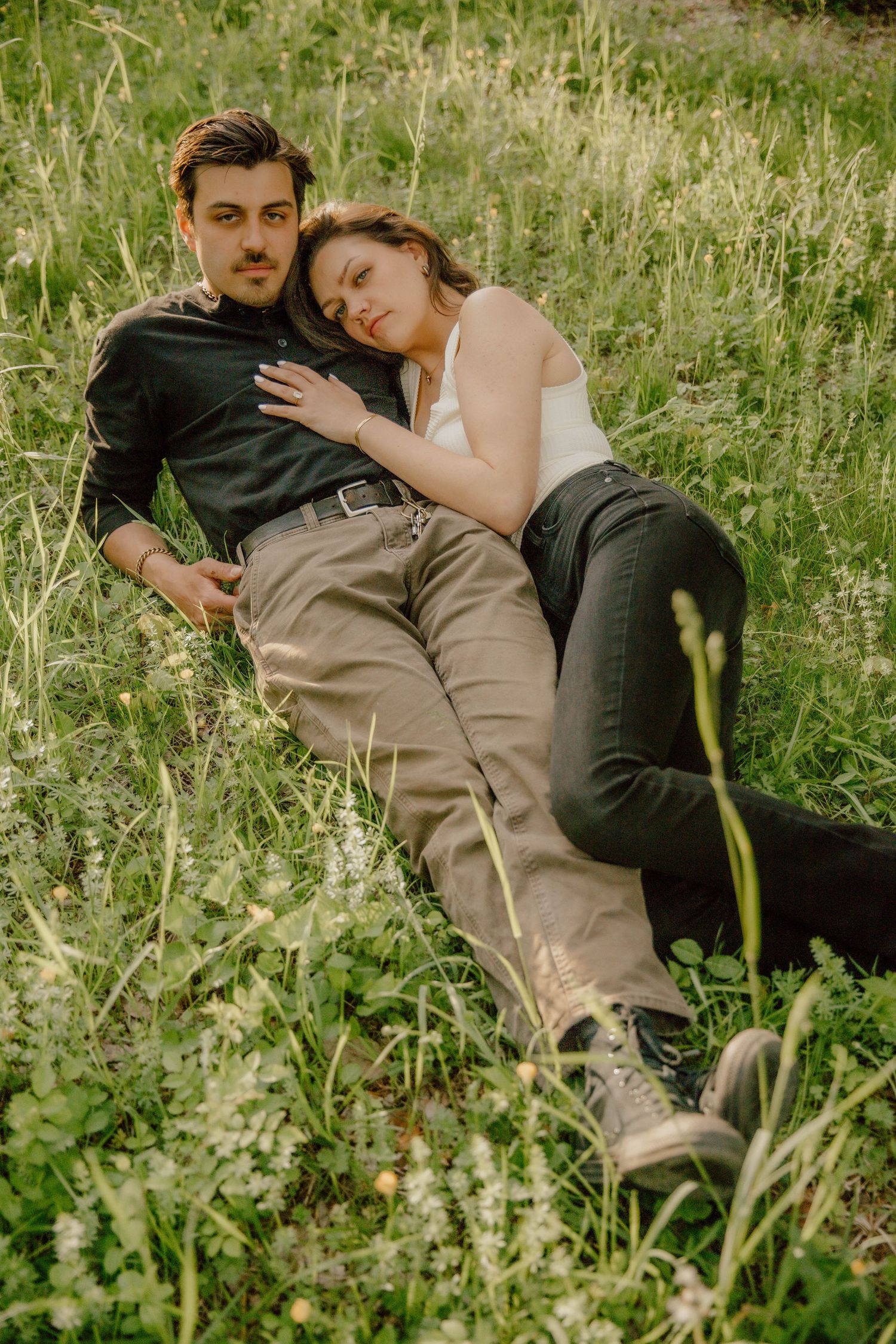 Young couple relaxing together in a lush green meadow filled with wildflowers at golden hour.