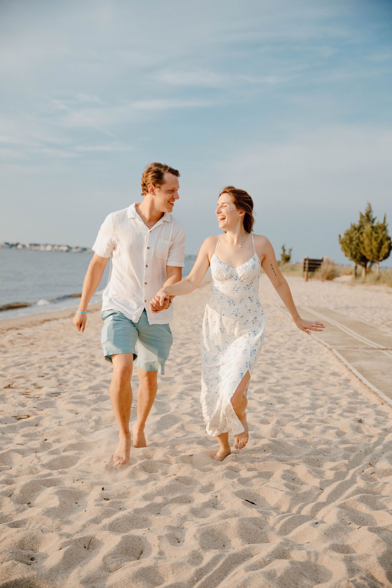 A happy couple runs hand in hand along a sandy beach on a sunny day.