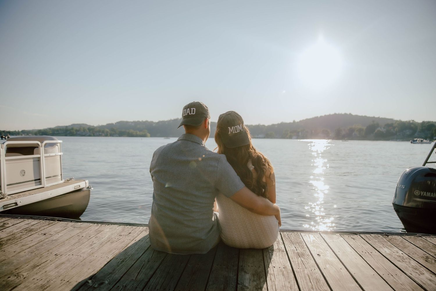 Couple sitting on a wooden dock embracing while watching a serene sunset over a calm lake.