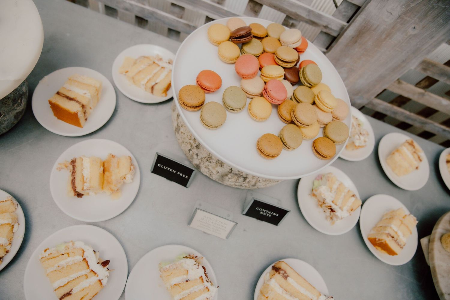 Overhead view of a dessert table with colorful macarons on a cake stand and plates of white cake slices.