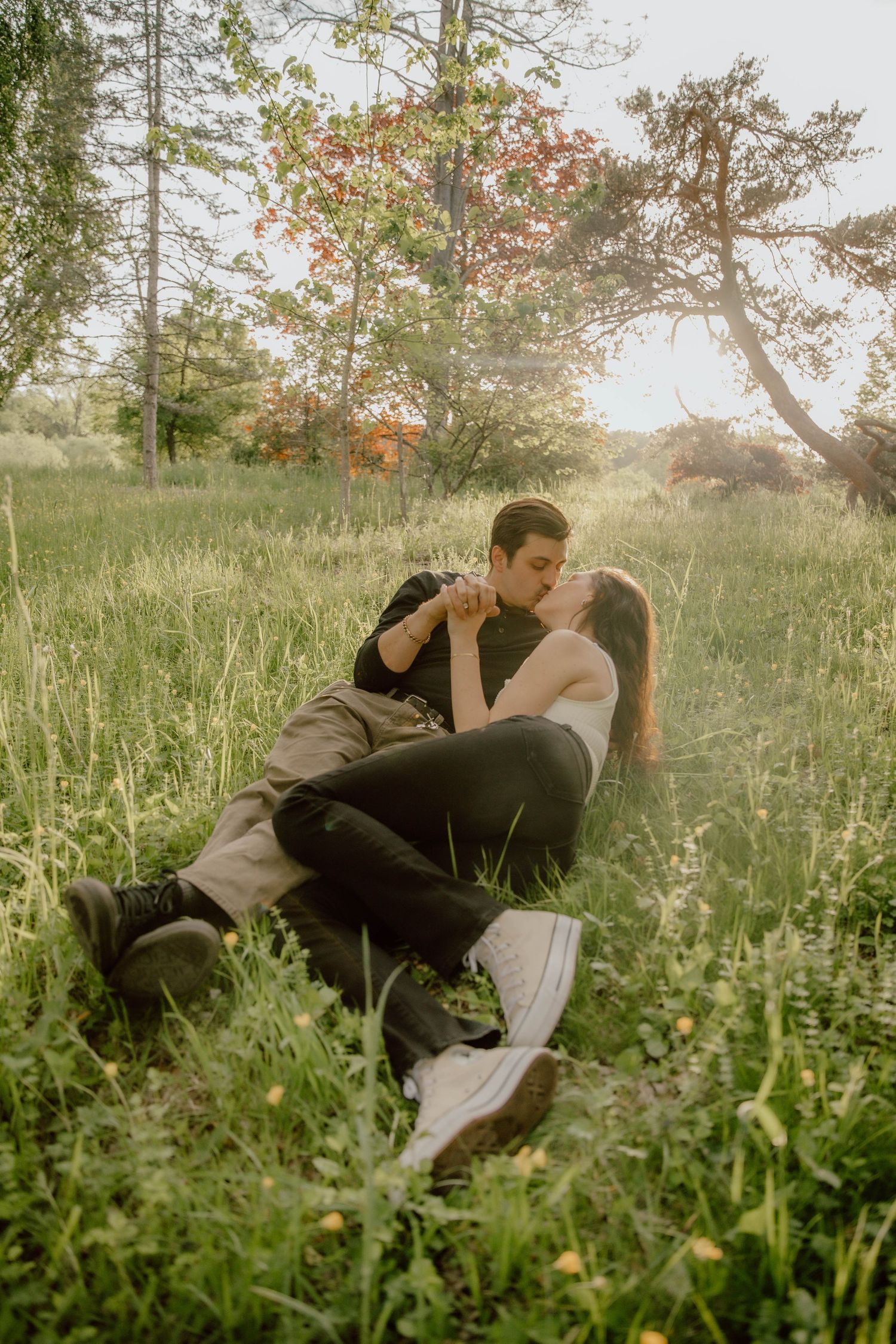Couple sharing a tender kiss while relaxing together in a sunlit meadow with tall grass.