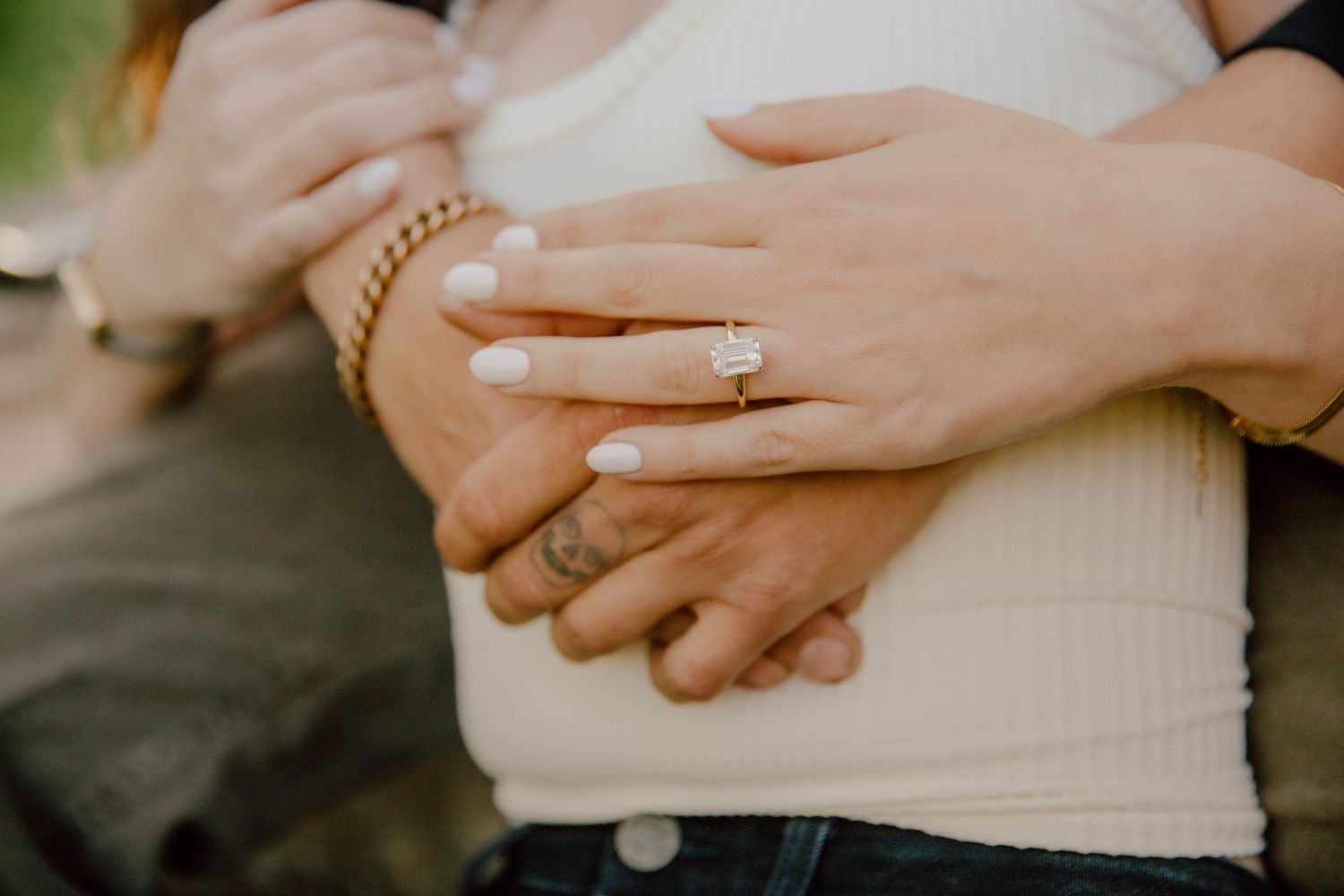 Close-up of engagement ring on woman's hand with white nails wrapped around partner's waist.
