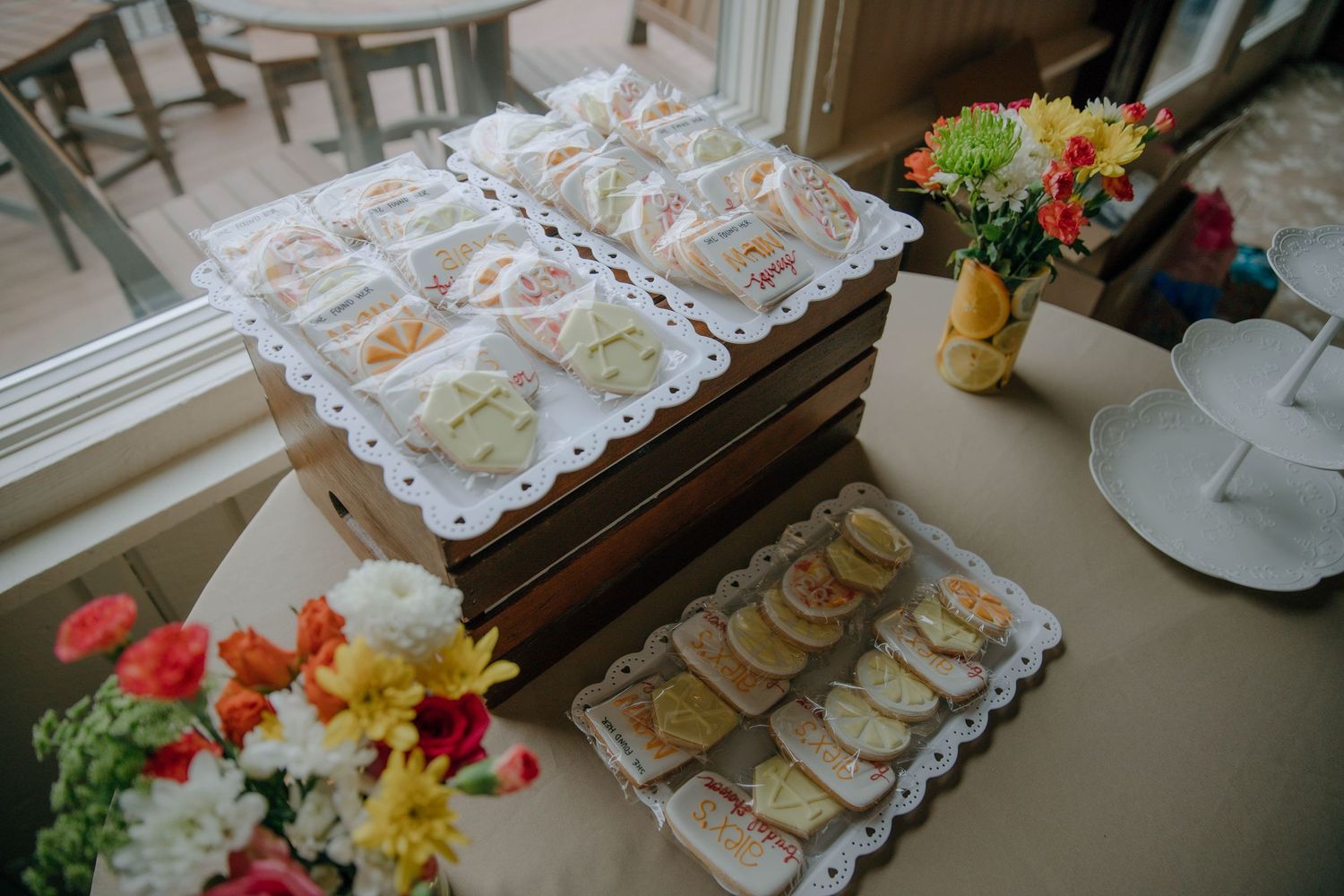 Elegant tea party spread with finger sandwiches on tiered wooden stand, cookies, and colorful flower arrangements on a table.