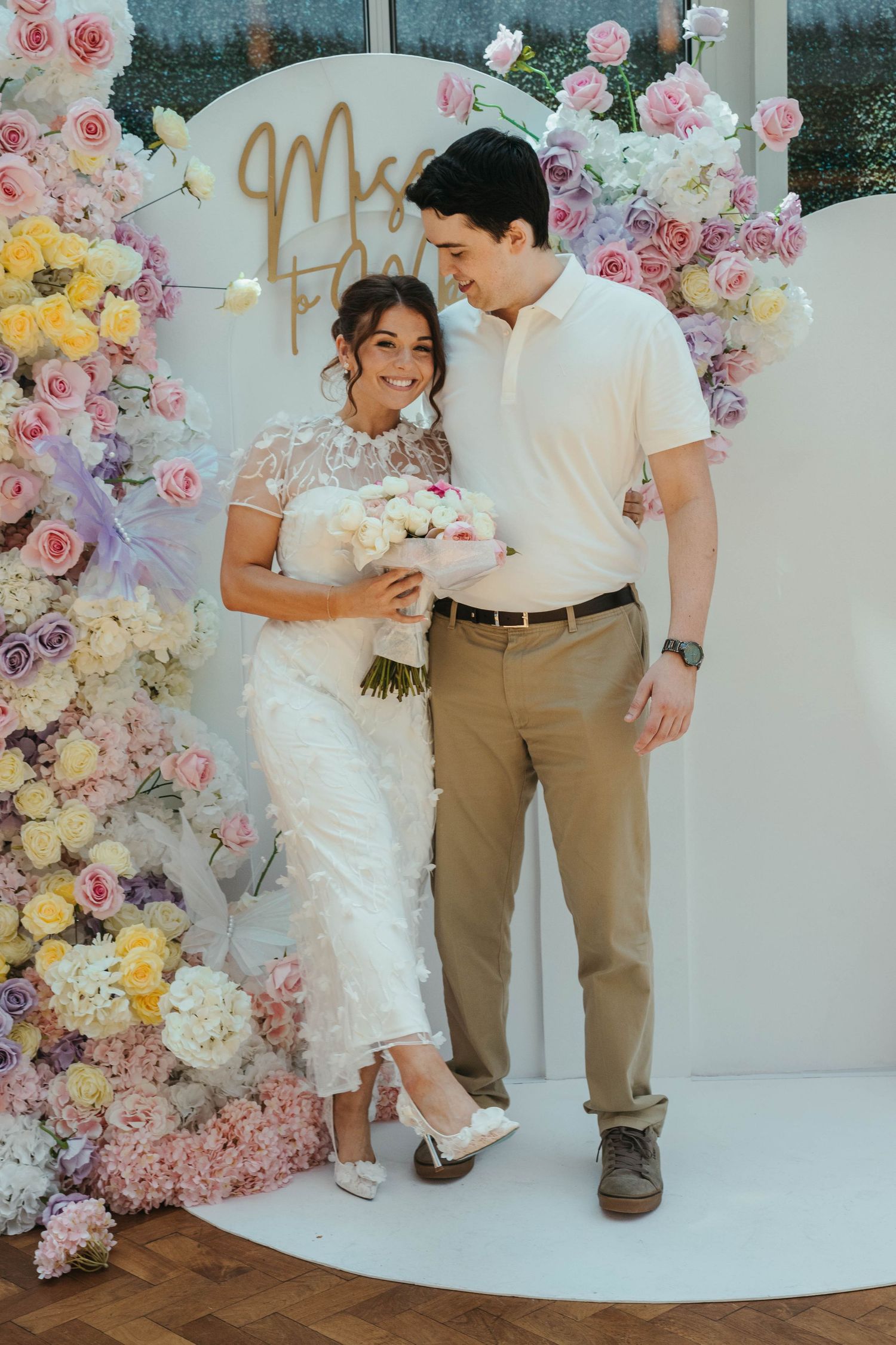Happy couple posing together in front of colorful floral backdrop at wedding celebration.