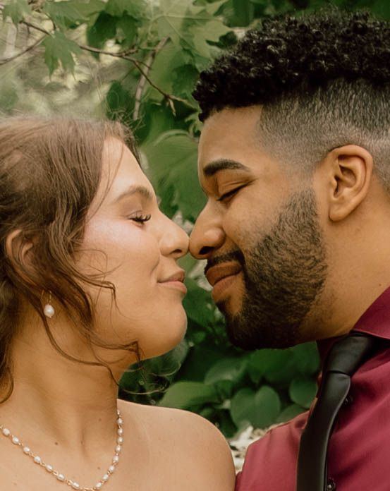 Bride and groom share intimate close moment surrounded by lush green foliage at outdoor wedding.