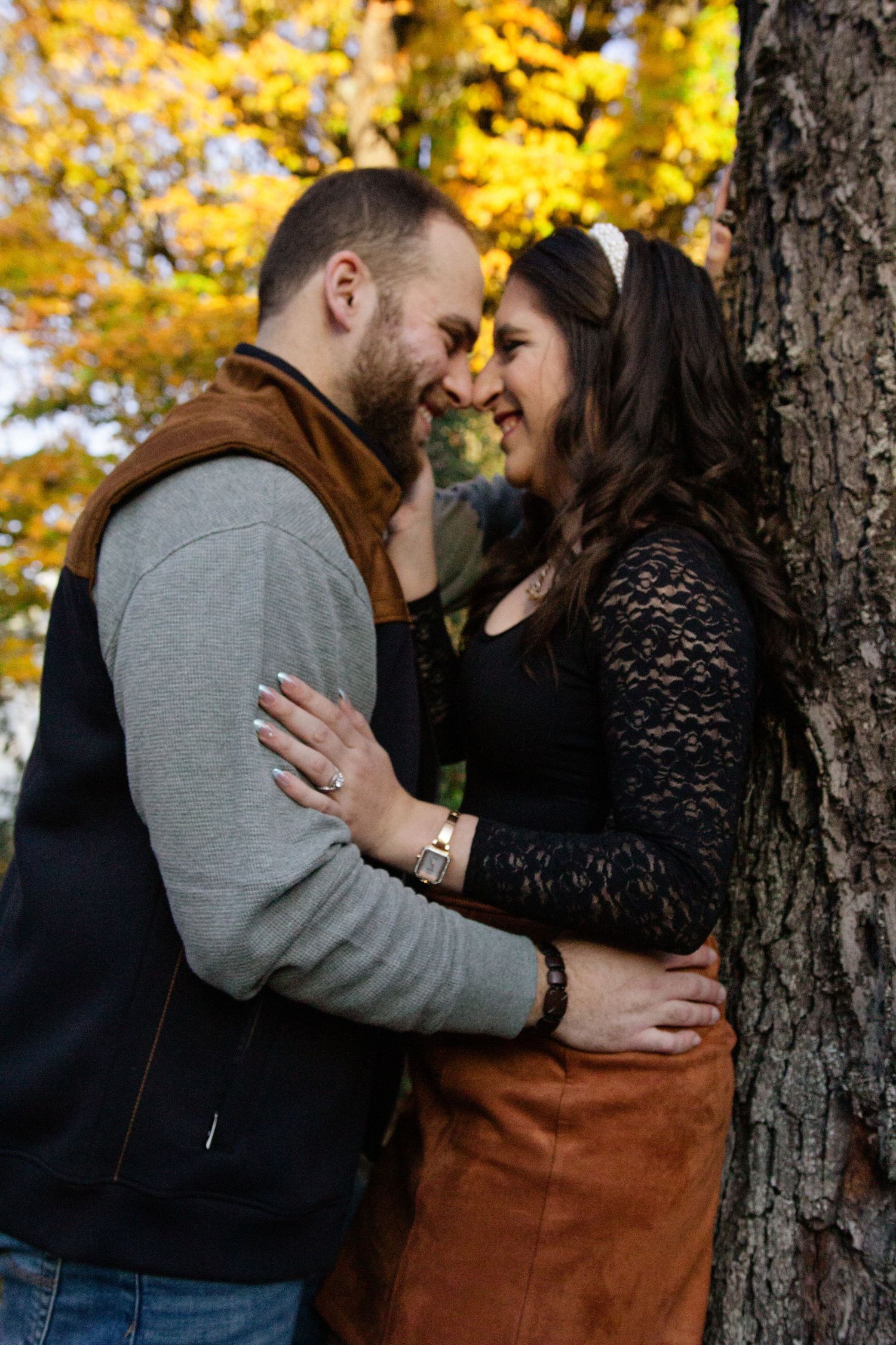 Happy couple embracing and smiling nose-to-nose beside a tree with vibrant yellow autumn foliage.