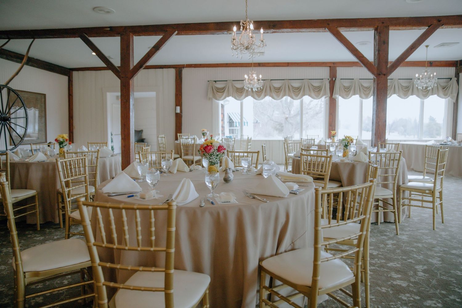 Elegant wedding reception hall with gold Chiavari chairs, round tables with champagne linens, and a crystal chandelier.