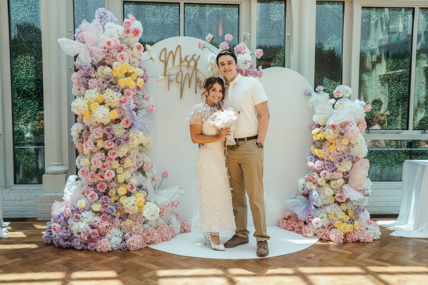 Couple posing in front of colorful floral arch with Mr & Mrs sign at wedding reception.