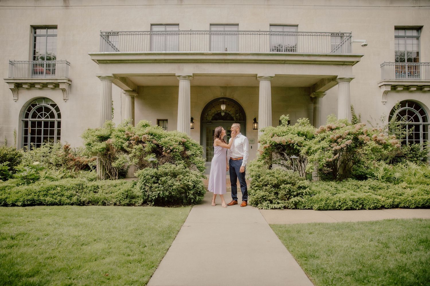 Couple standing together on a garden path in front of a grand historic mansion.