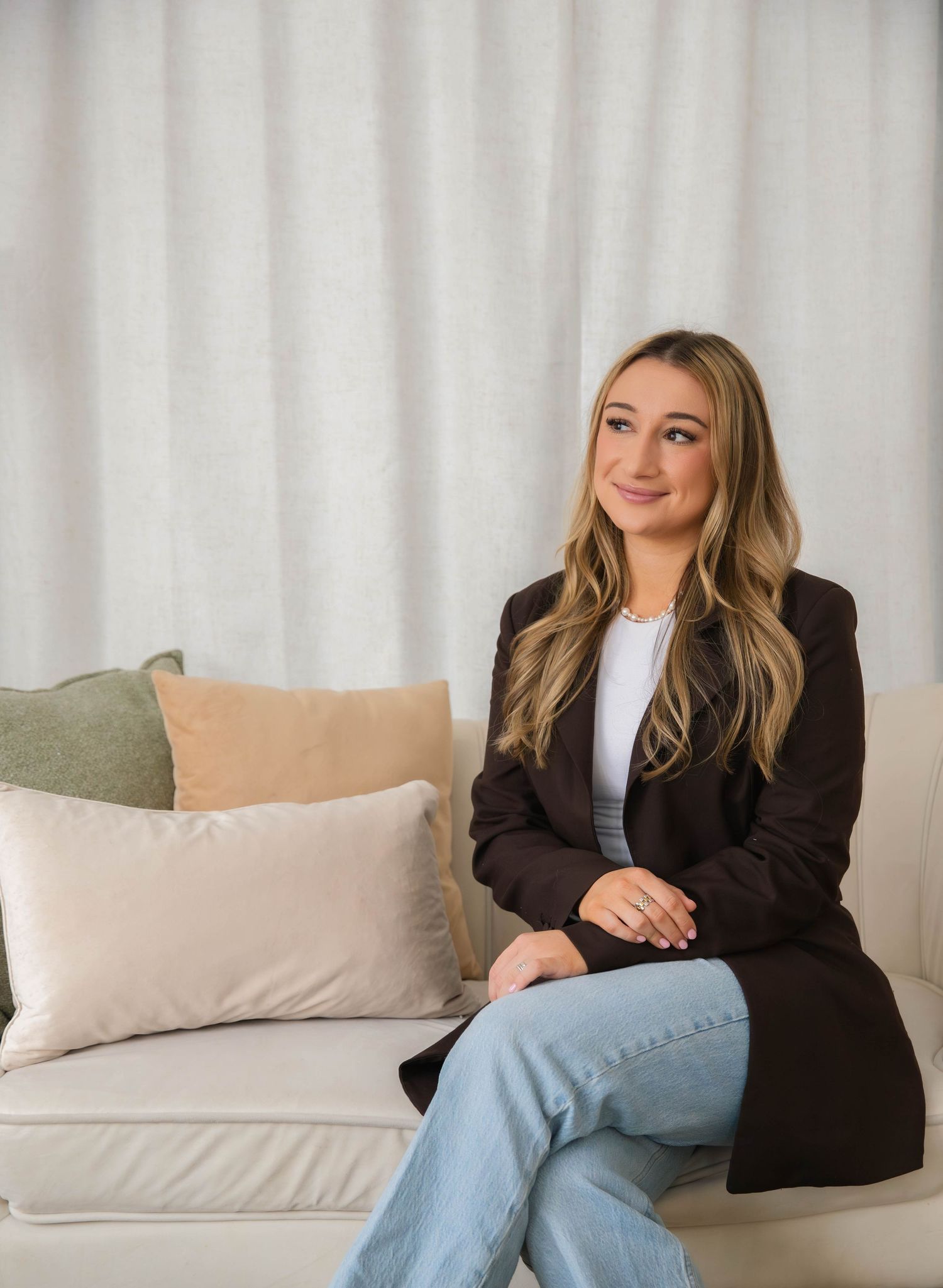 Professional woman in blazer sitting confidently on a couch in a bright, modern setting.
