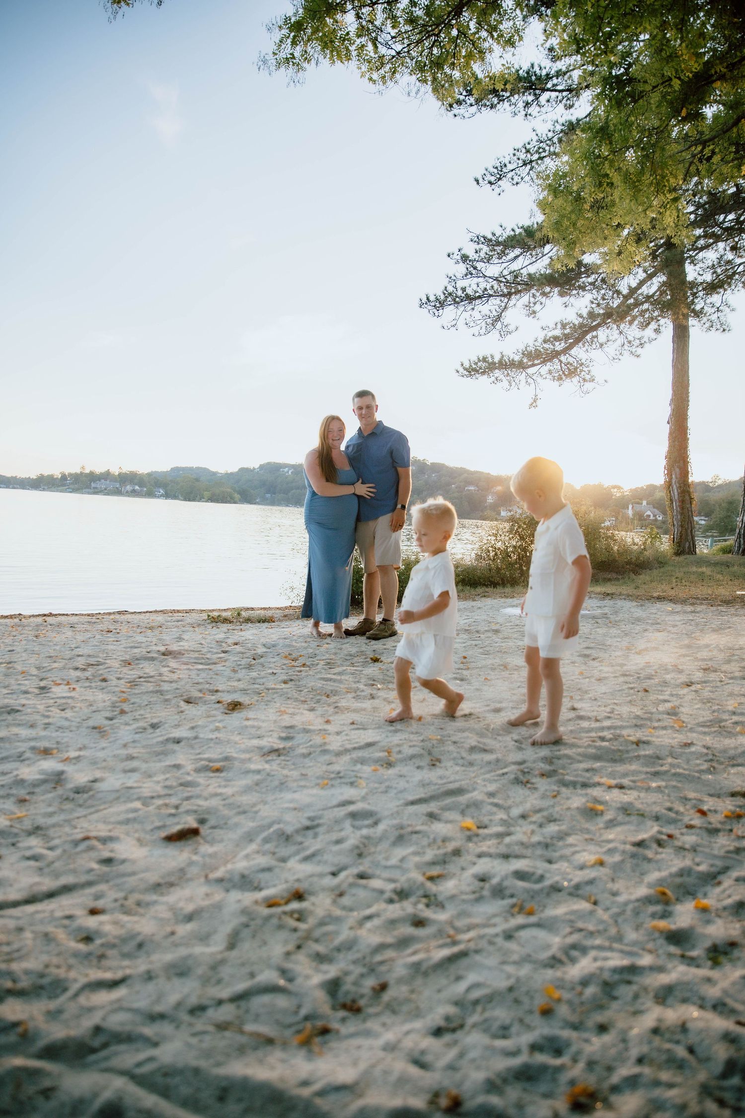 Family of four enjoying a sunny day on a sandy lakeside beach at golden hour.