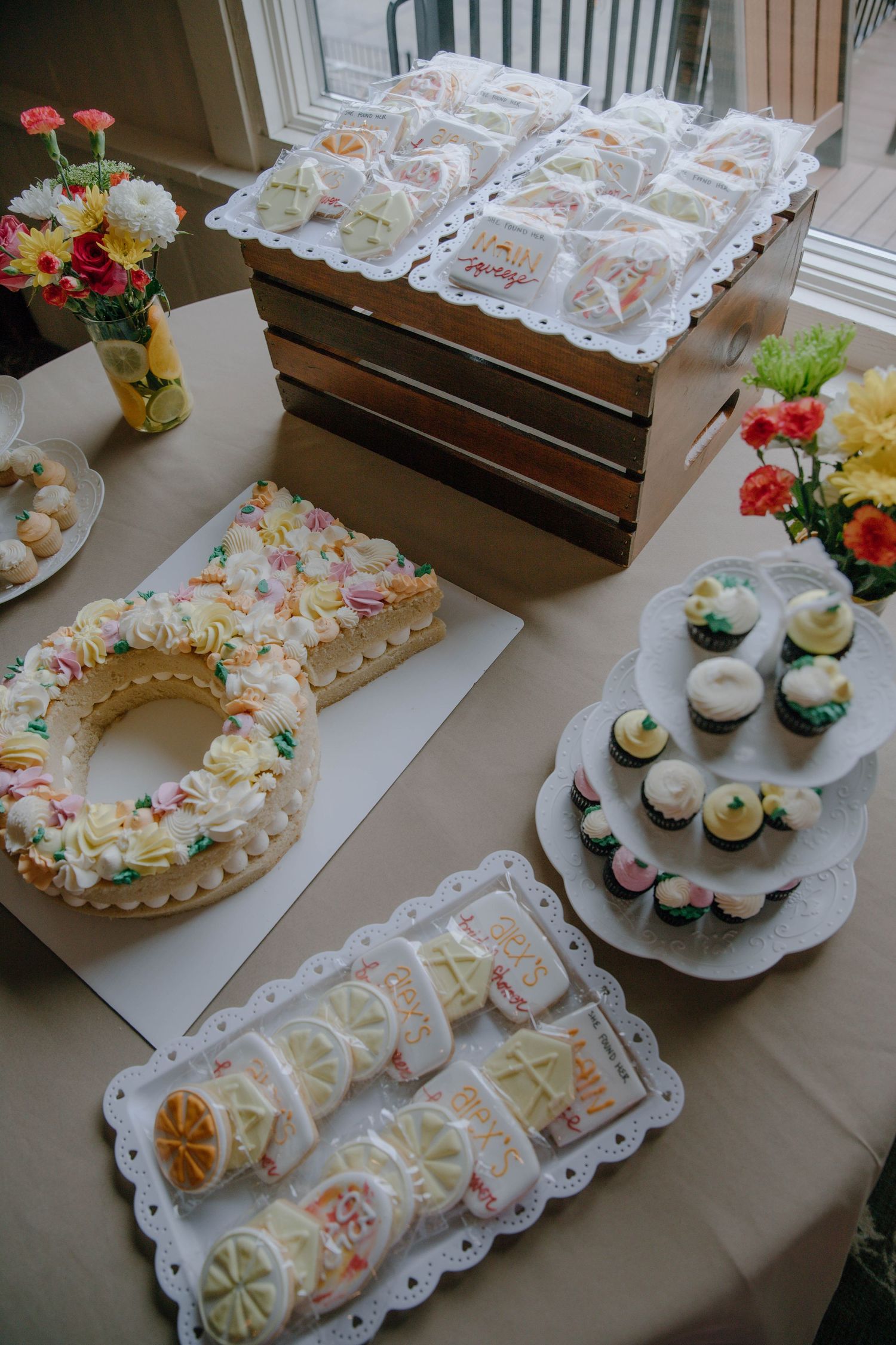 Dessert table featuring letter-shaped cake, cupcakes, and decorated cookies at a celebration party.