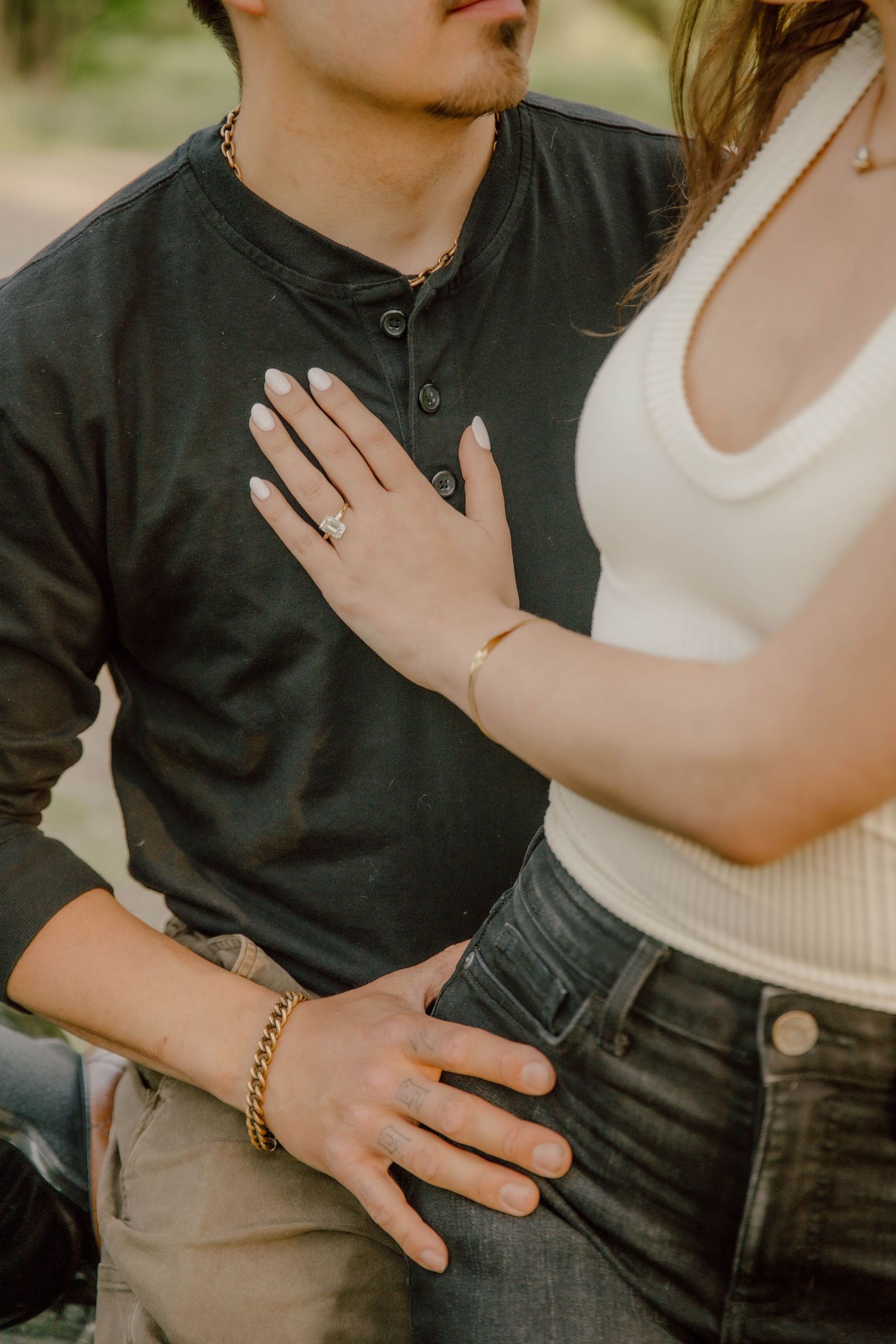 Close-up of couple holding hands, woman wearing engagement ring and gold bracelets.