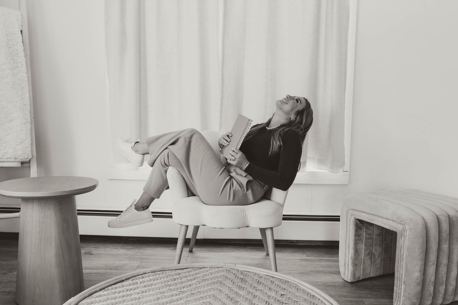 Woman relaxing in modern white chair, black and white interior photography with curtains and minimalist furniture.