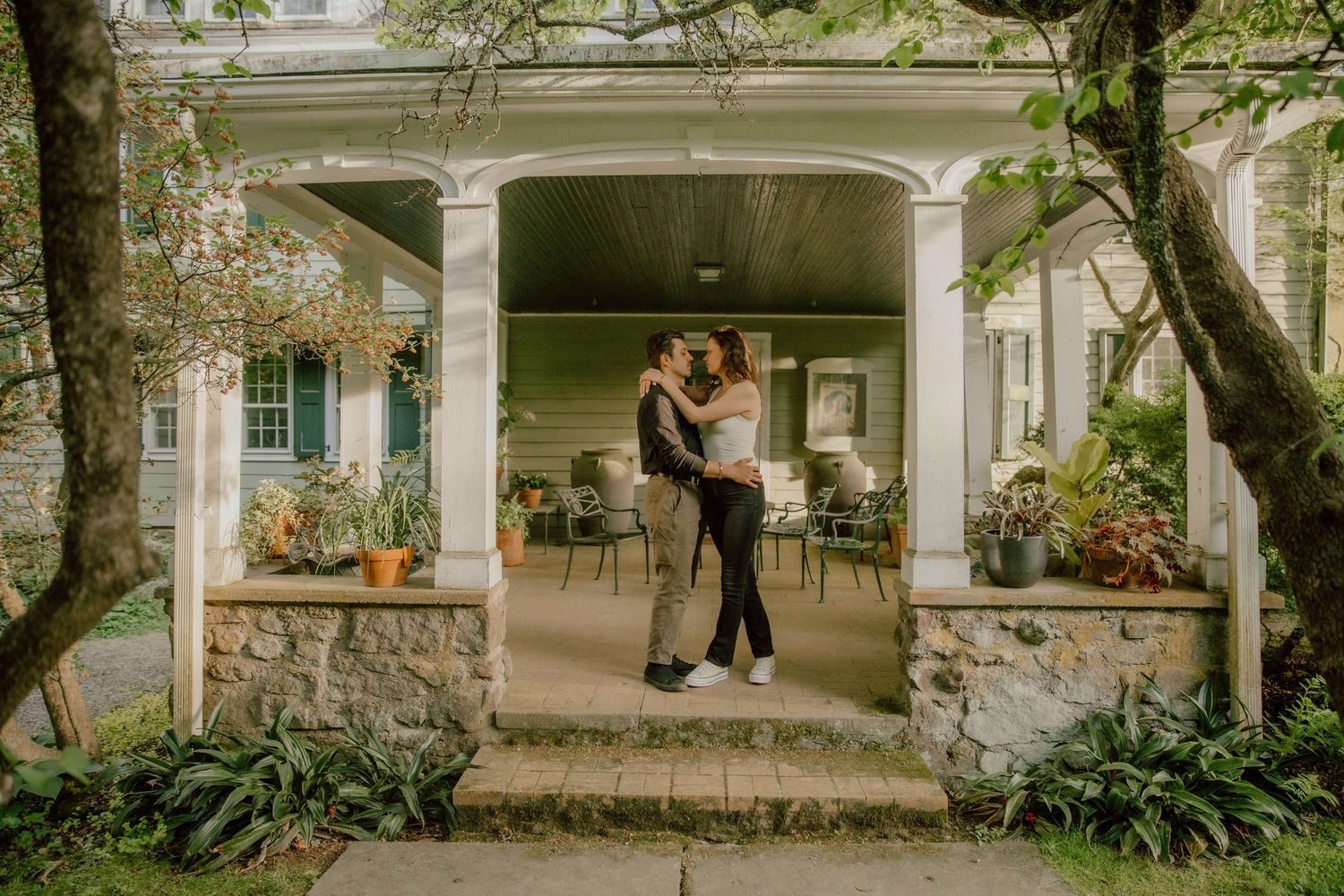 Couple dancing on a charming stone porch surrounded by lush greenery and potted plants.