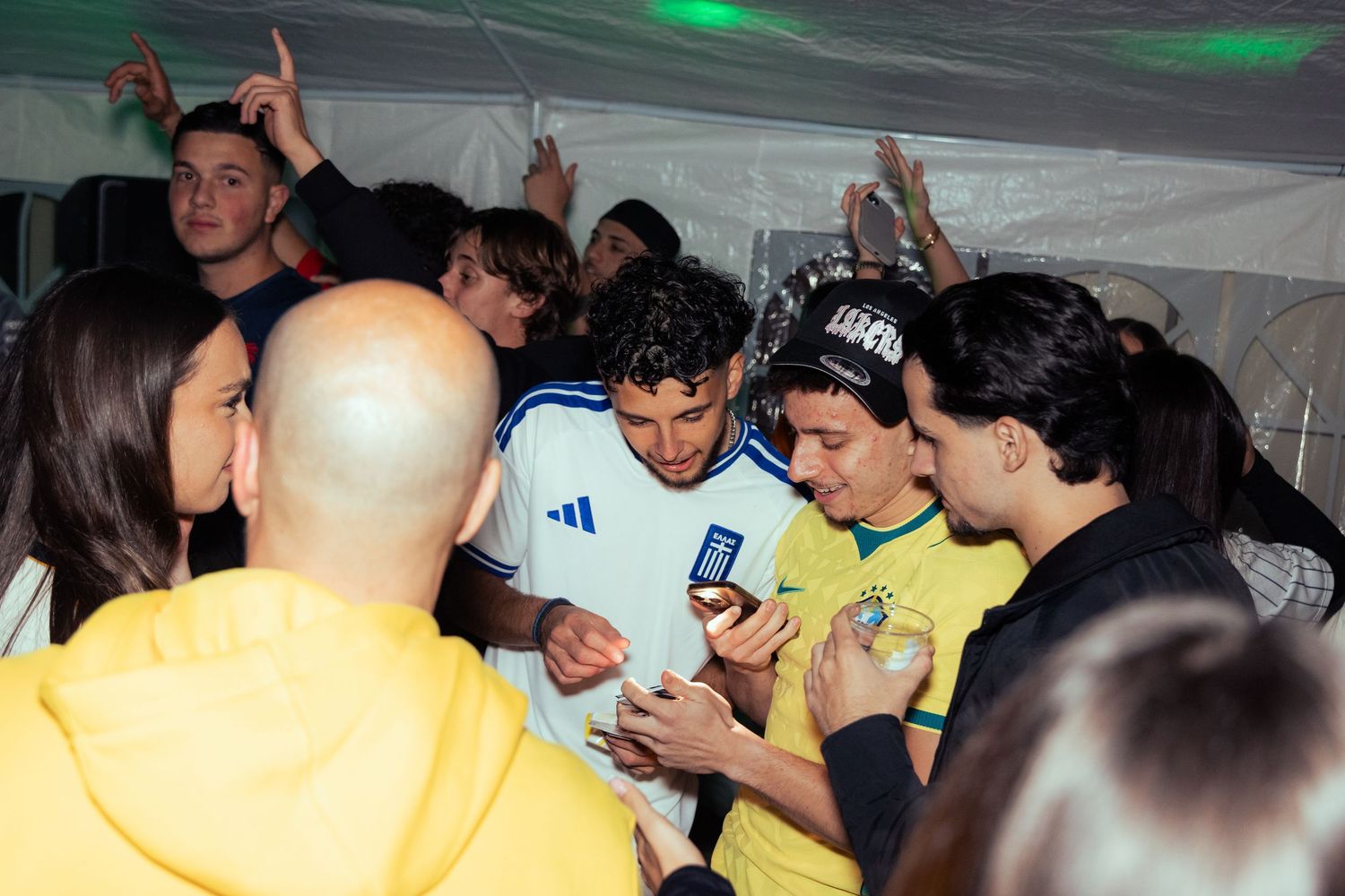 Group of young people gathered at an indoor event, with one person wearing a Brazil soccer jersey signing autographs.
