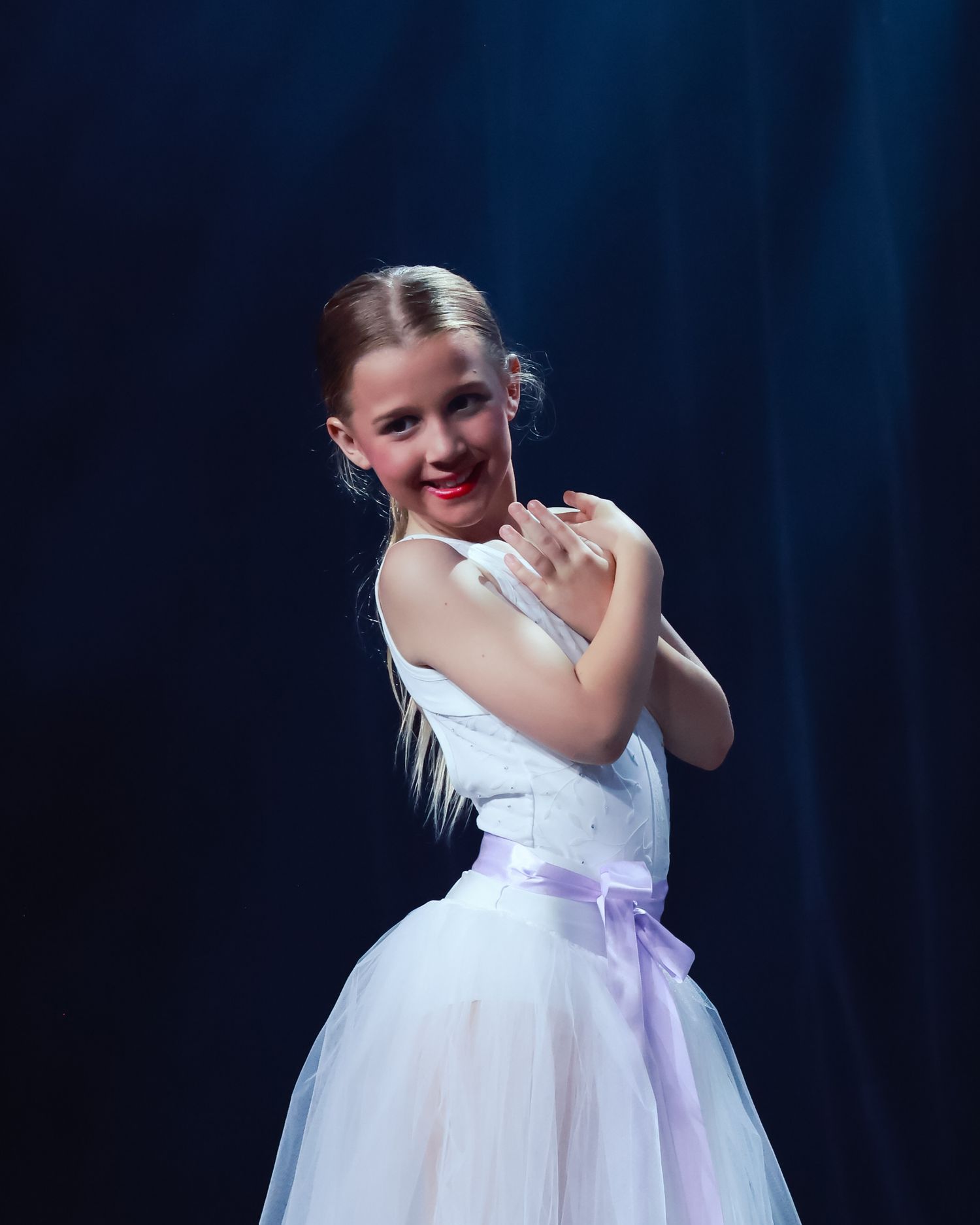 Sydney concert photographer concert photographer Dancer in white tutu with purple sash performs gracefully against blue stage lighting.