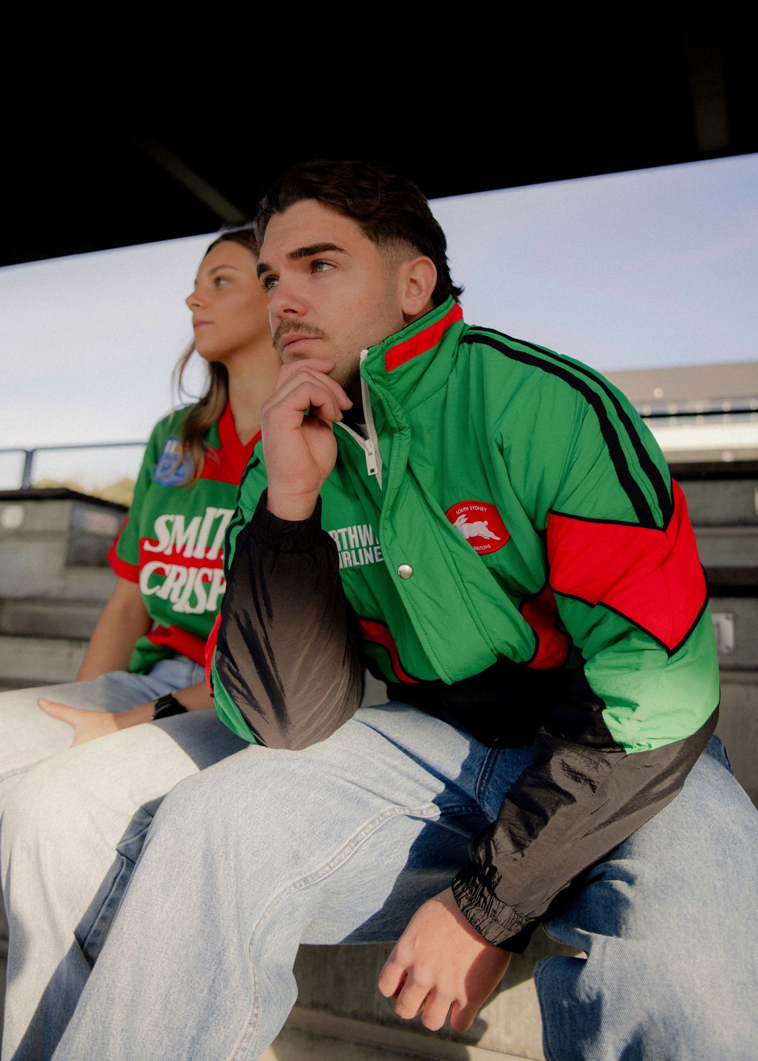 Two fans wearing green and red South Sydney Rabbitohs NRL jerseys sitting in stadium bleachers. Sutherland Shire videographer