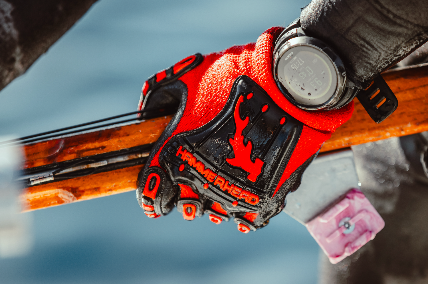 Close-up product photography of diver's hand holding orange and red spearfishing equipment.