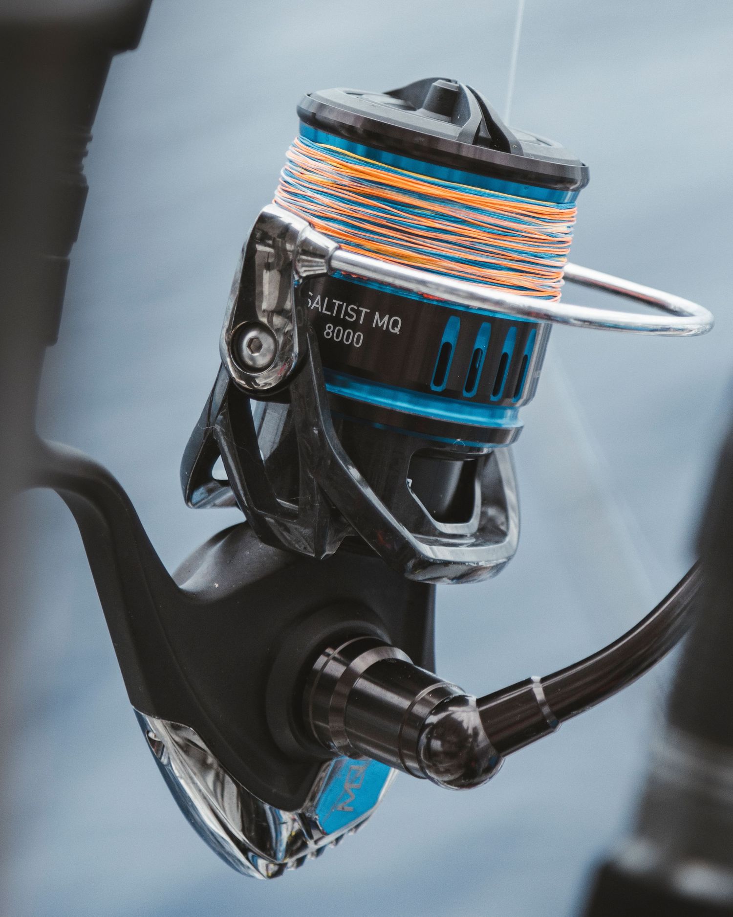 Close-up of a Daiwa Saltist MQ 8000 spinning fishing reel with colorful line on a rod.