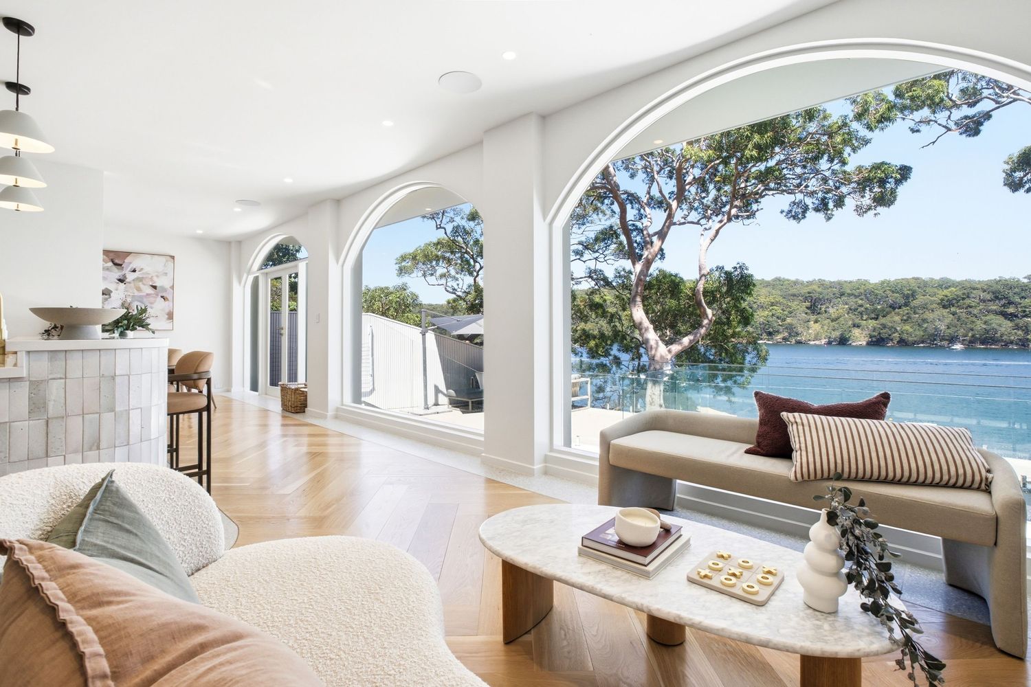 Bright living room with arched windows overlooking waterfront and lush trees, featuring neutral furnishings.