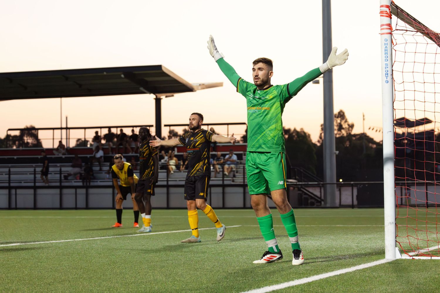 Wollongong sports photographer capturesSoccer goalkeeper in green uniform makes diving save at goal post during match.