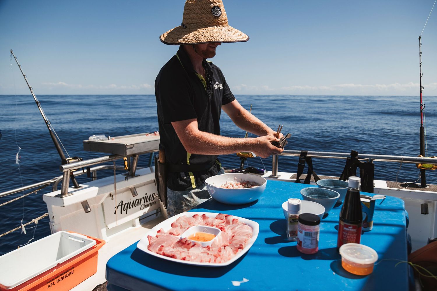 Angler preparing fresh bait on a boat table with fishing rods and ocean in the background.