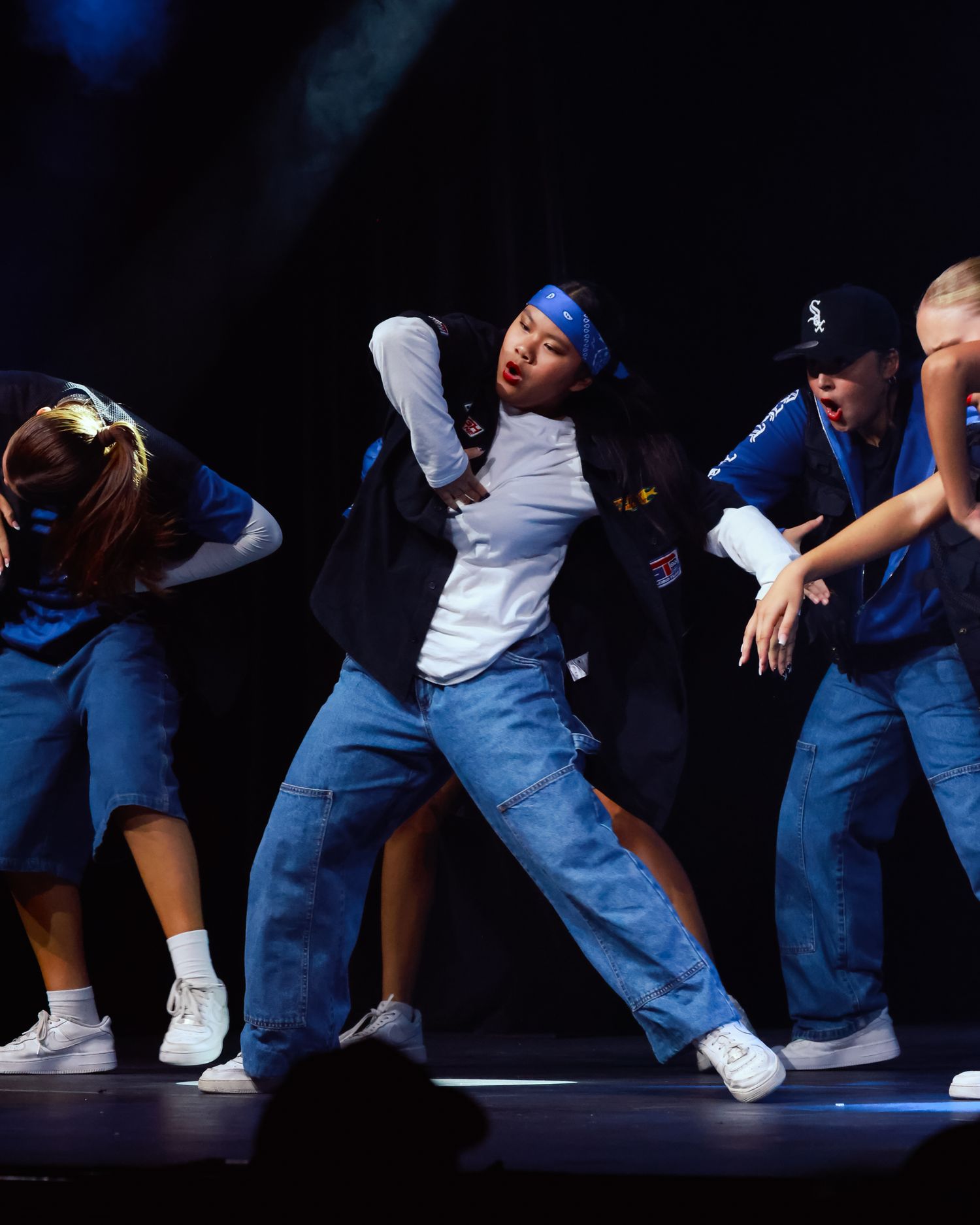 Sydney concert photographer Hip hop dancers in jeans and white sneakers perform low crouching moves on a dark stage.