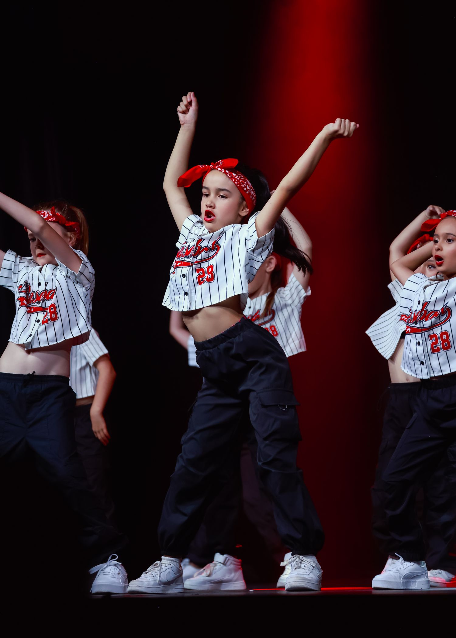 Sydney concert photographer Dance performers in baseball-style outfits execute energetic moves against a dark red background.