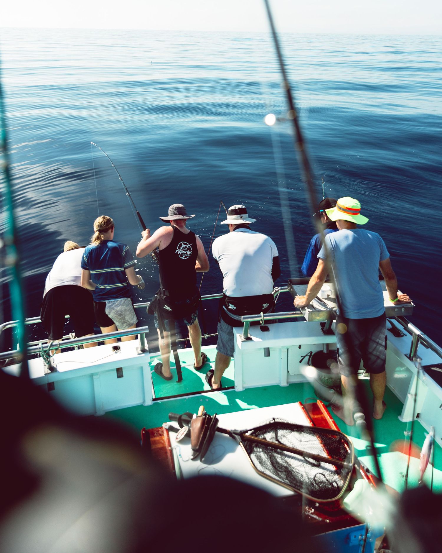 Group of men deep sea fishing from a boat on calm blue ocean waters on a sunny day.
