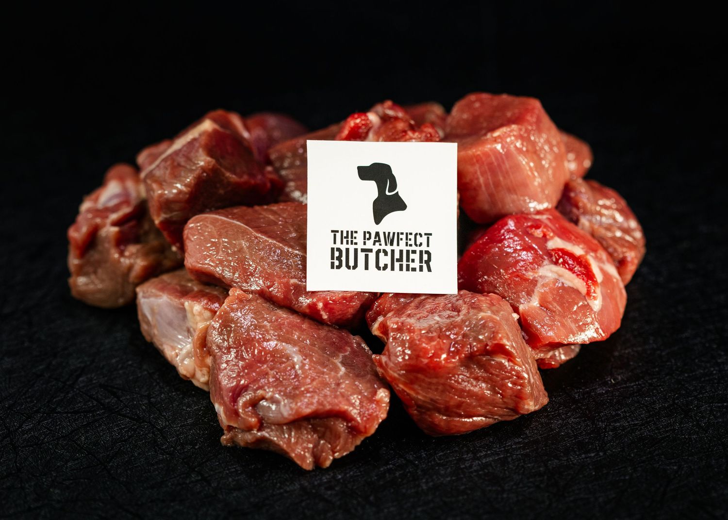 Product photography Food and product photography and videography Raw red meat chunks arranged around a butcher shop logo on black surface.