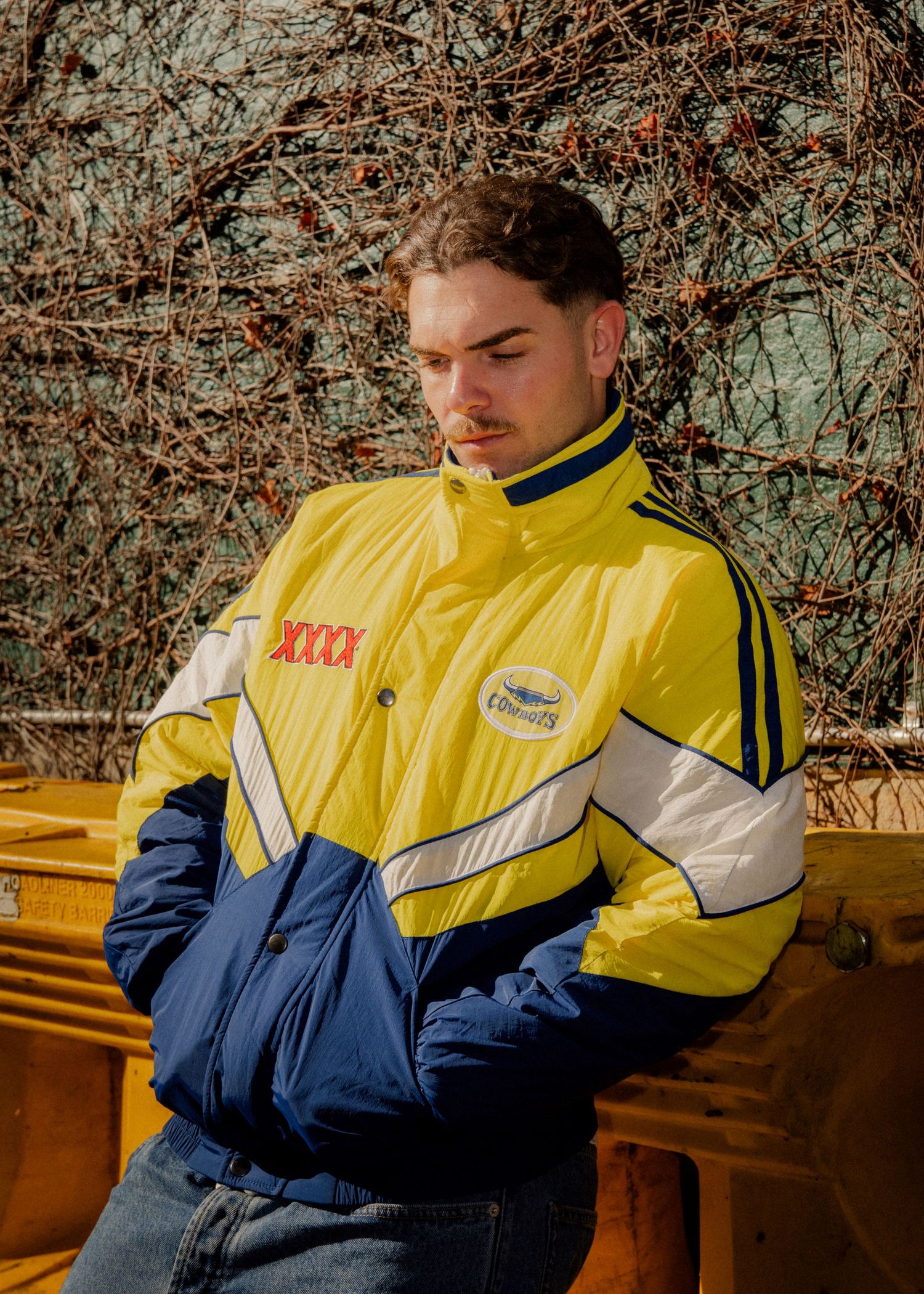 Young man wearing a yellow and navy XXXX Parramatta Eels vintage NRL jacket poses outdoors in sunlight. Sutherland videographer