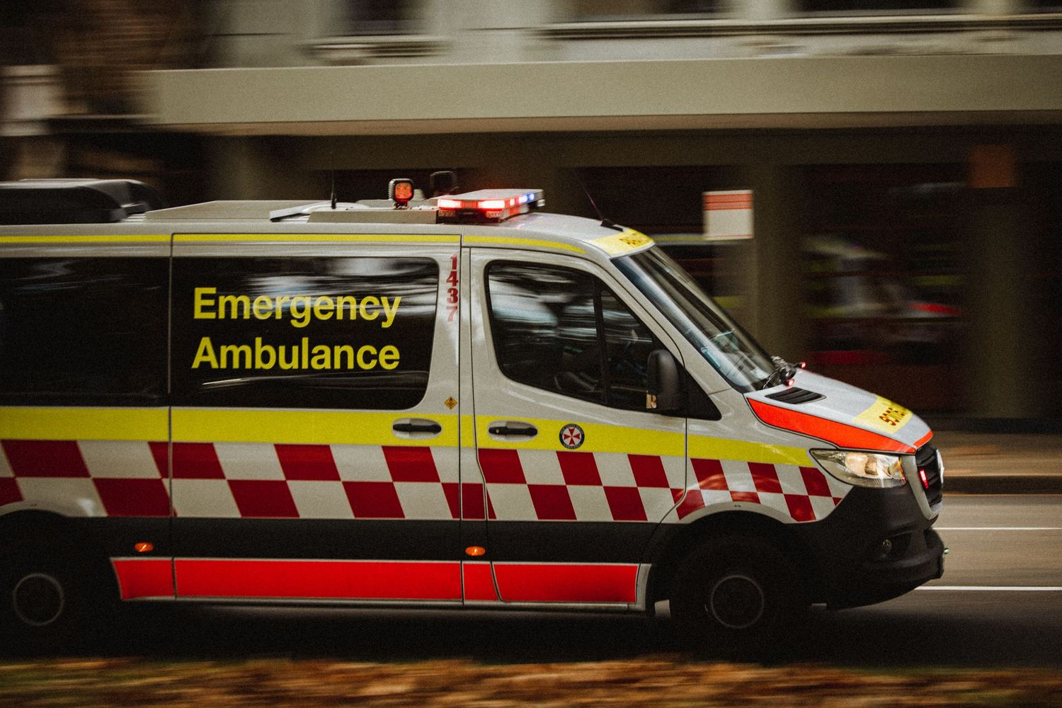An emergency ambulance with red and yellow markings speeds down a city street with motion blur in the background. Sutherland Shire photograp