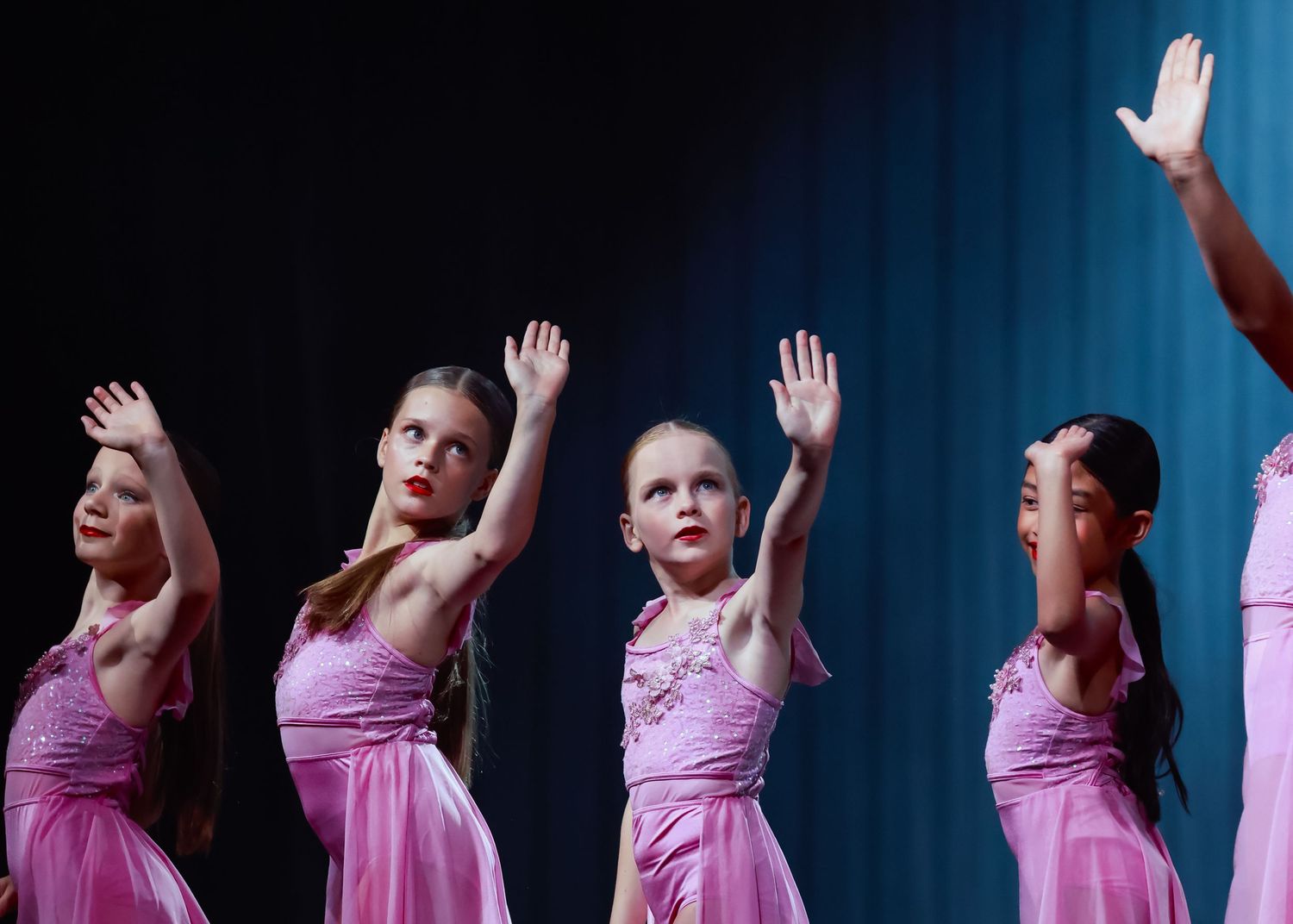 Wollongong dance and concert photographer Dancers in pink dresses perform synchronized arm movements against blue stage lighting.