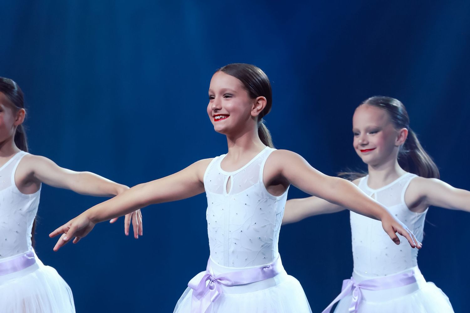 Sydney concert photographer Ballet dancers in white tutus with purple sashes perform graceful arm movements on stage.