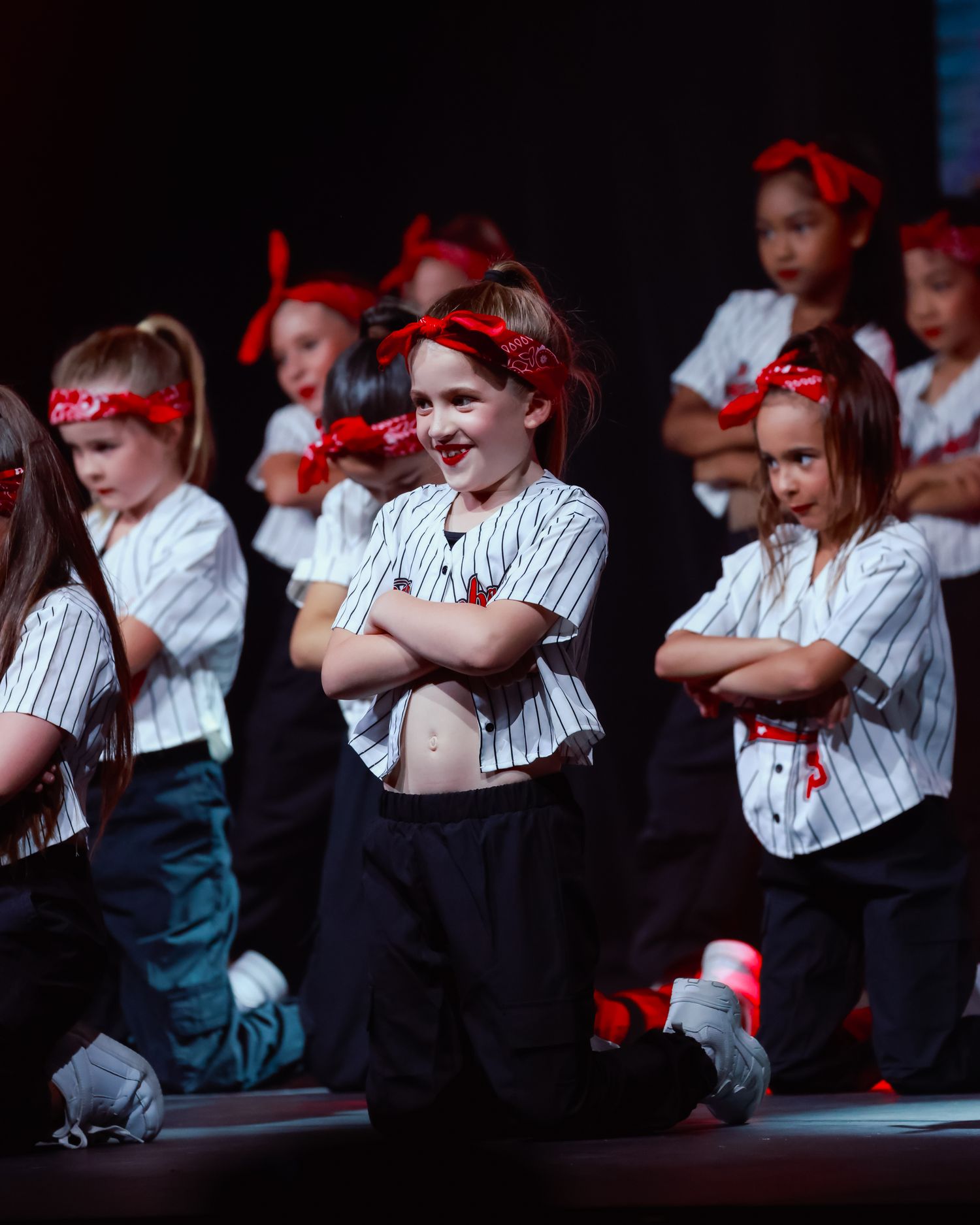 Dance concert photography of Young performers in striped uniforms with red accessories sit in a row during a stage production in Sutherland