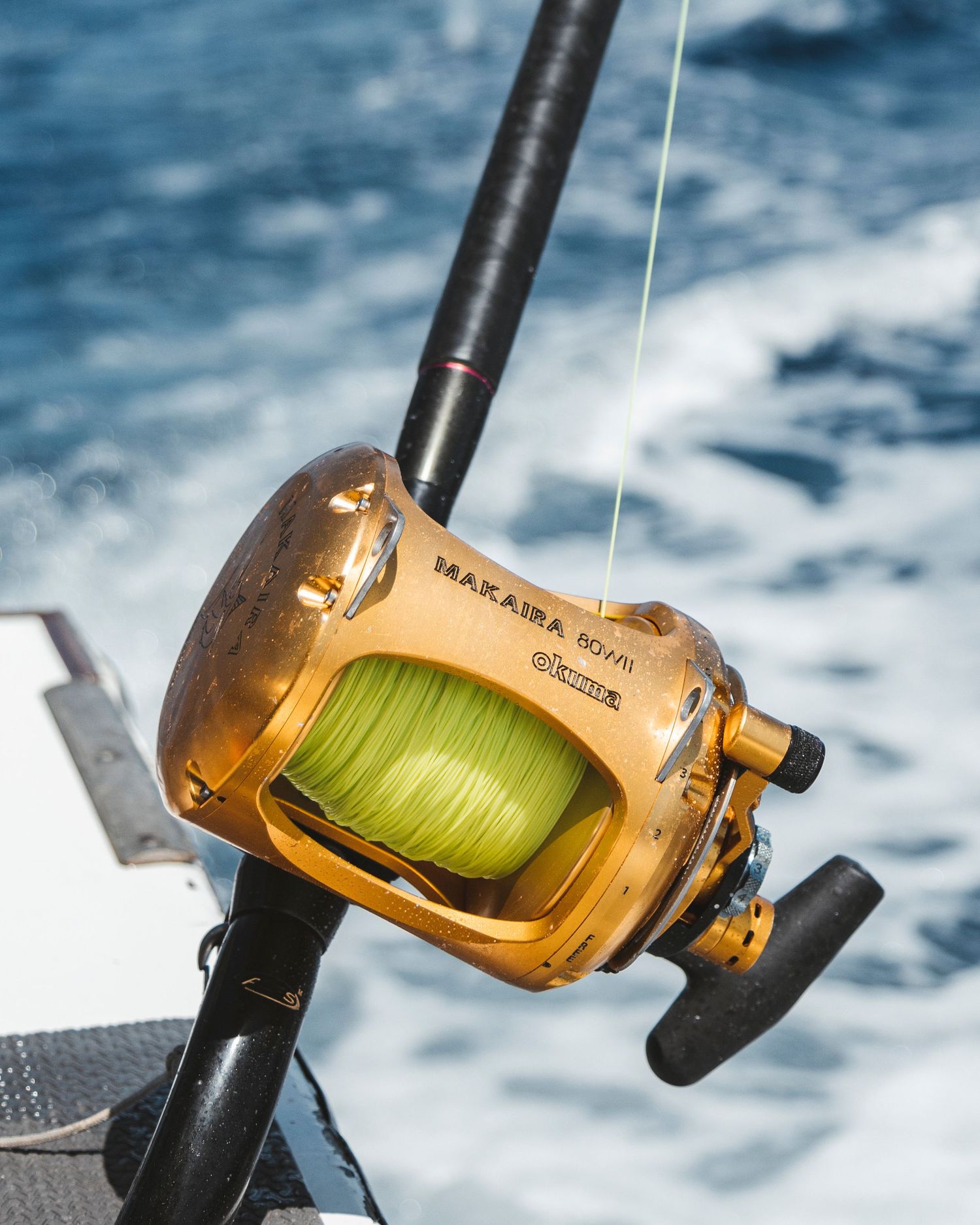 Gold Okuma Makaira fishing reel with green line mounted on a rod on a deep sea fishing boat.