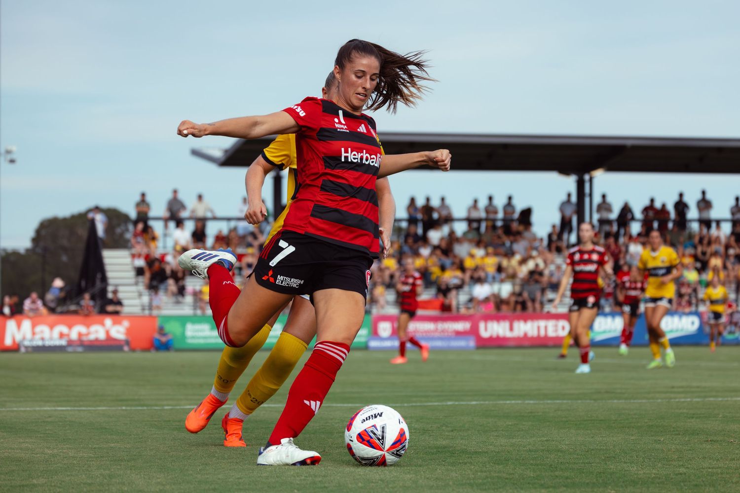 Sydney sports photographer captures player in red and black striped jersey dribbles ball during competitive match.