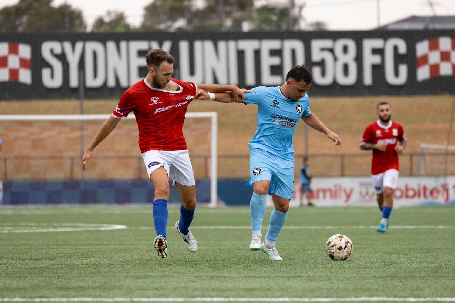 Sydney sports photographer captures Soccer players from opposing teams competing for ball during match at Sydney United stadium.