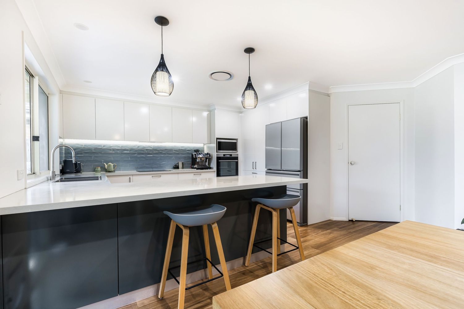 Modern kitchen with black island, white cabinetry, pendant lights, and bar stools on timber floors.