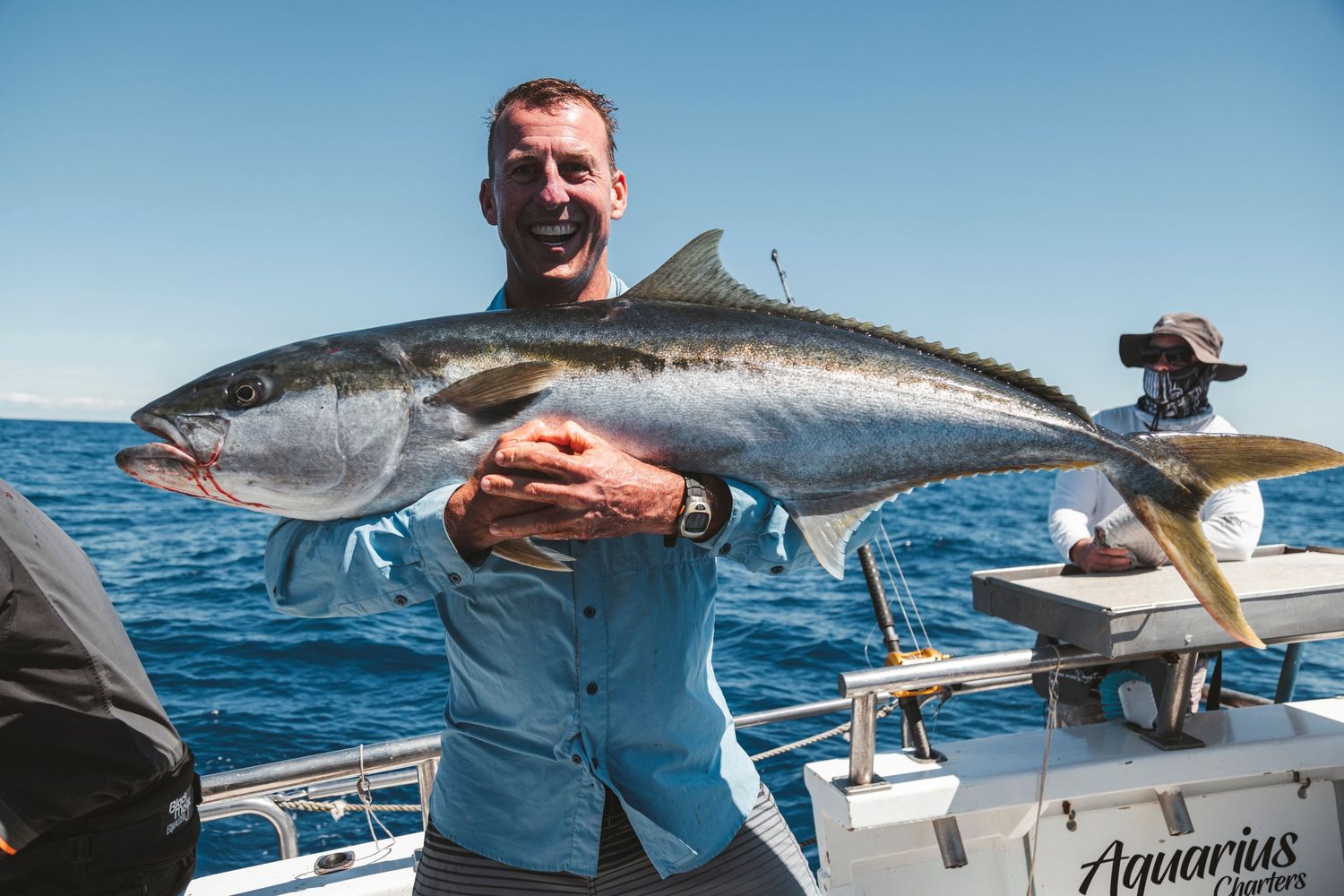 Smiling man holding a large kingfish on a fishing charter boat on a sunny day at sea.