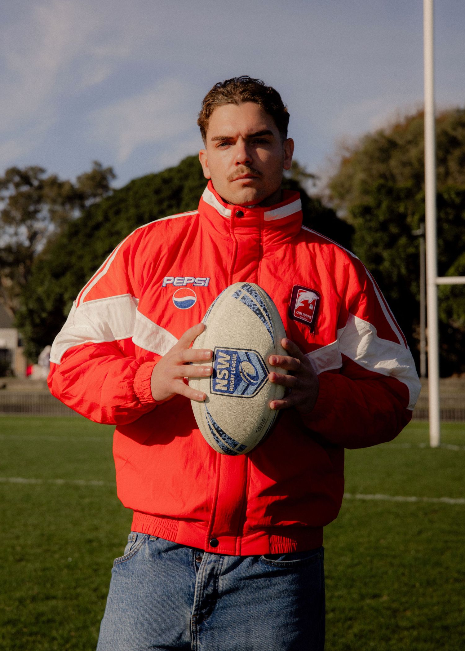 Young man on rugby field holding NSW football, wearing a red and white Pepsi-branded sports jacket. Business and brand photographer sydney