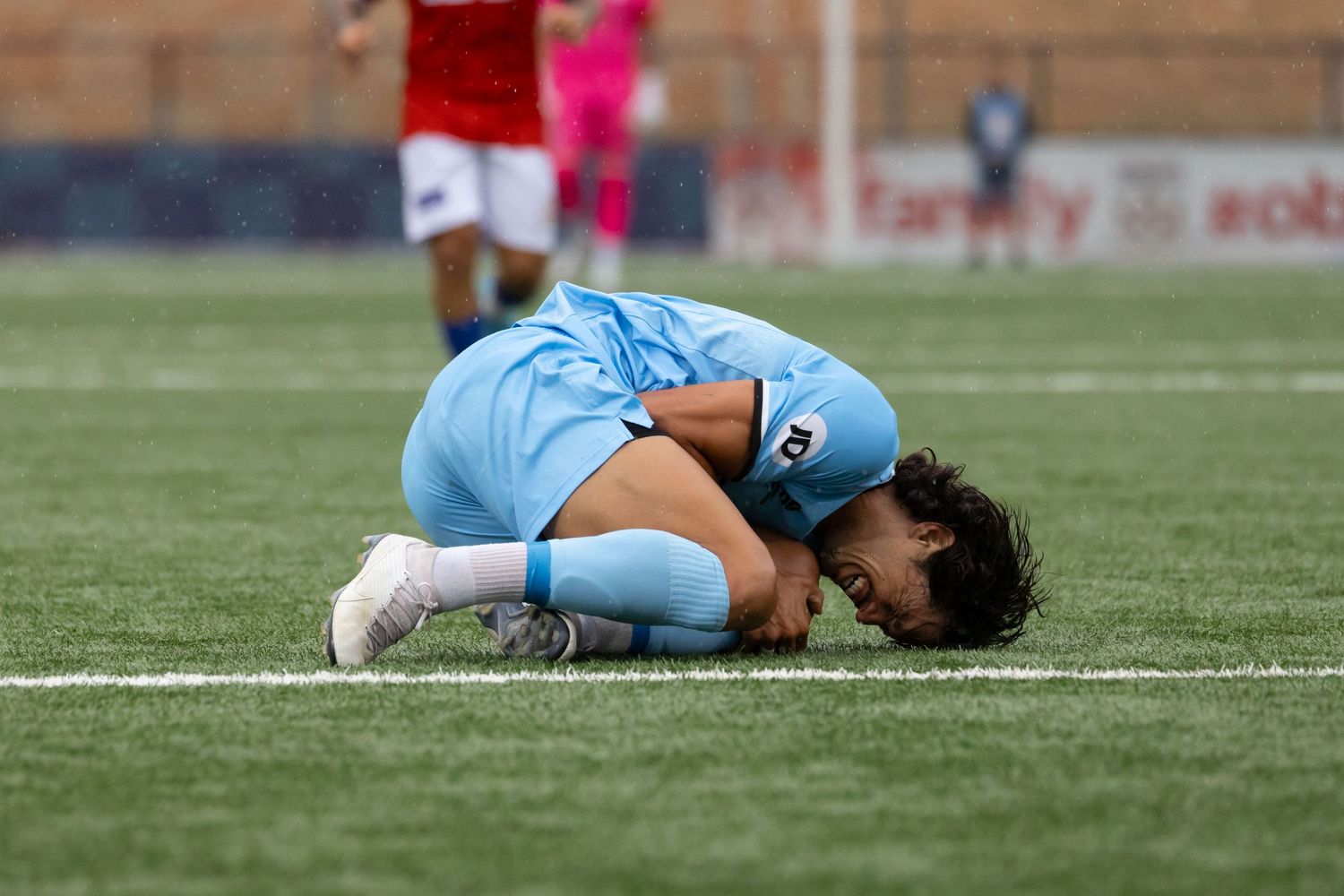 Sutherland Shire based sports photographer captures Soccer player in light blue uniform lying on ground in apparent distress.